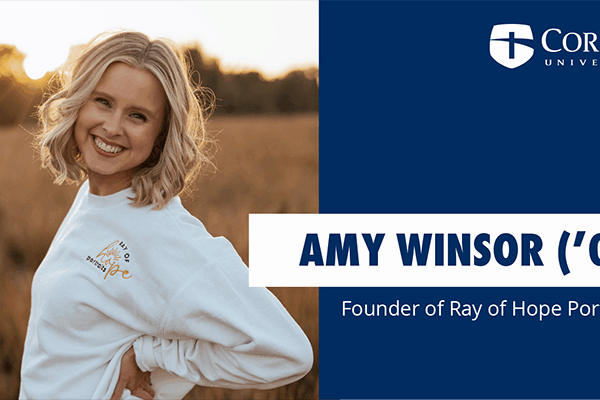 A person smiling stands outdoors in a field, wearing a white sweatshirt. The text on the right reads: Corban University, Amy Winsor (09), and Founder of Ray of Hope Portraits.