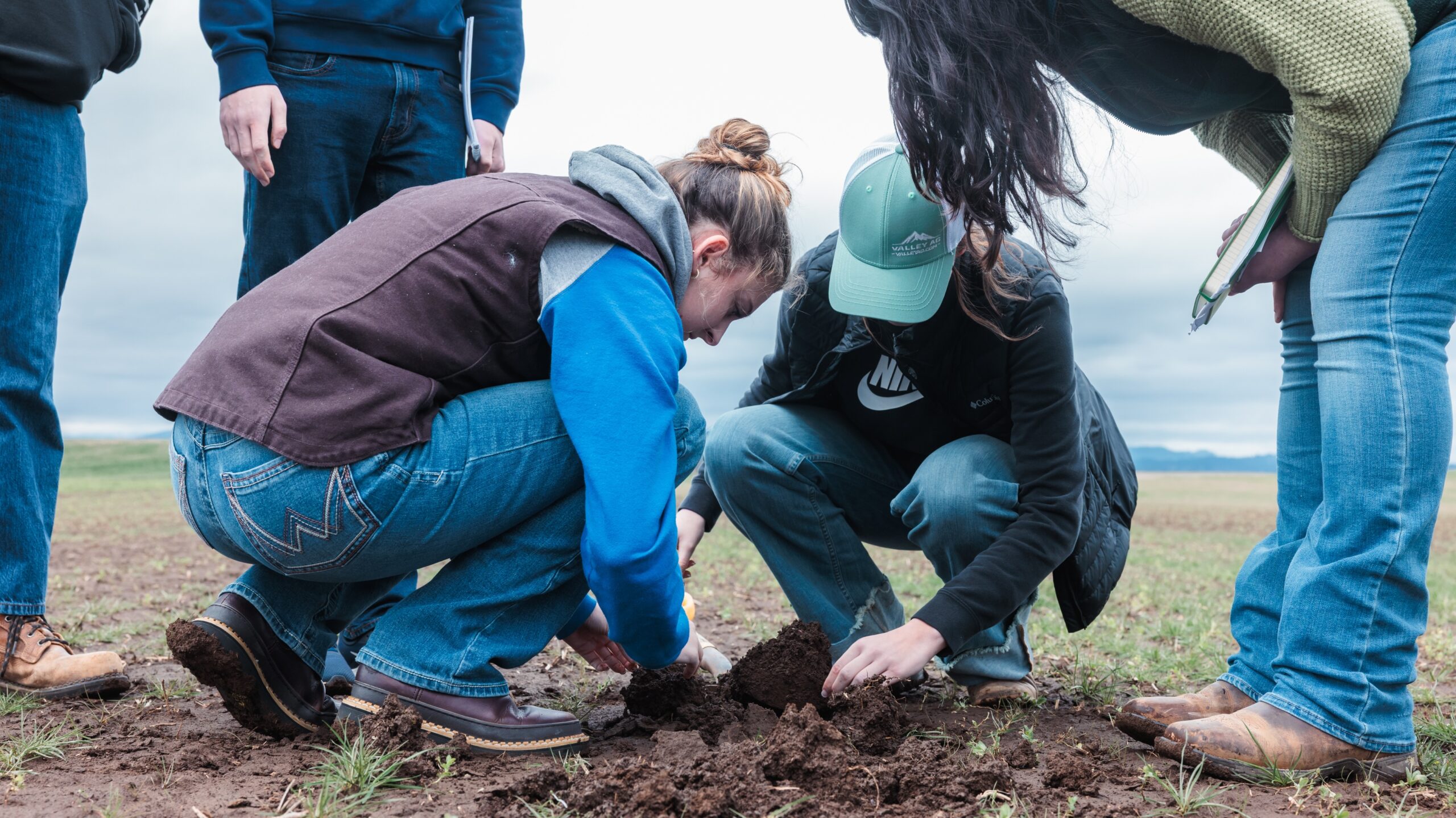 A group of students kneeling in dirt, engaged in an activity, with focused expressions on their faces.