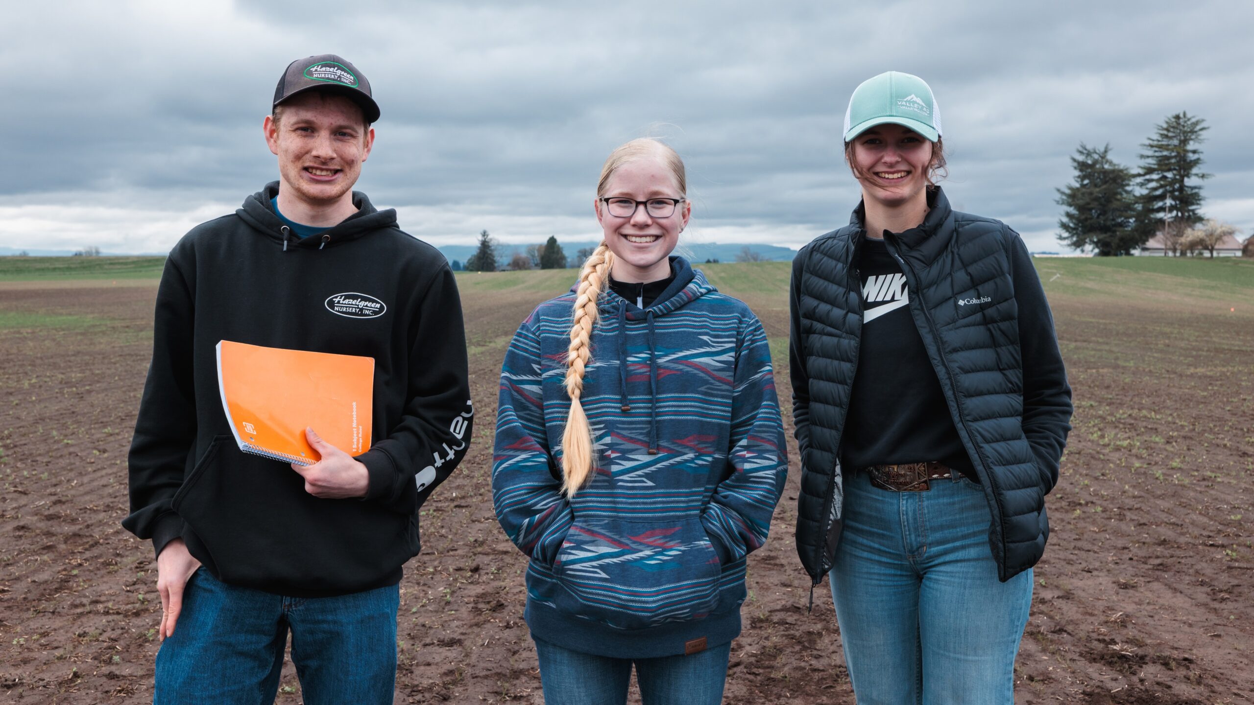 Three students, one man and two women, standing in a crop field.