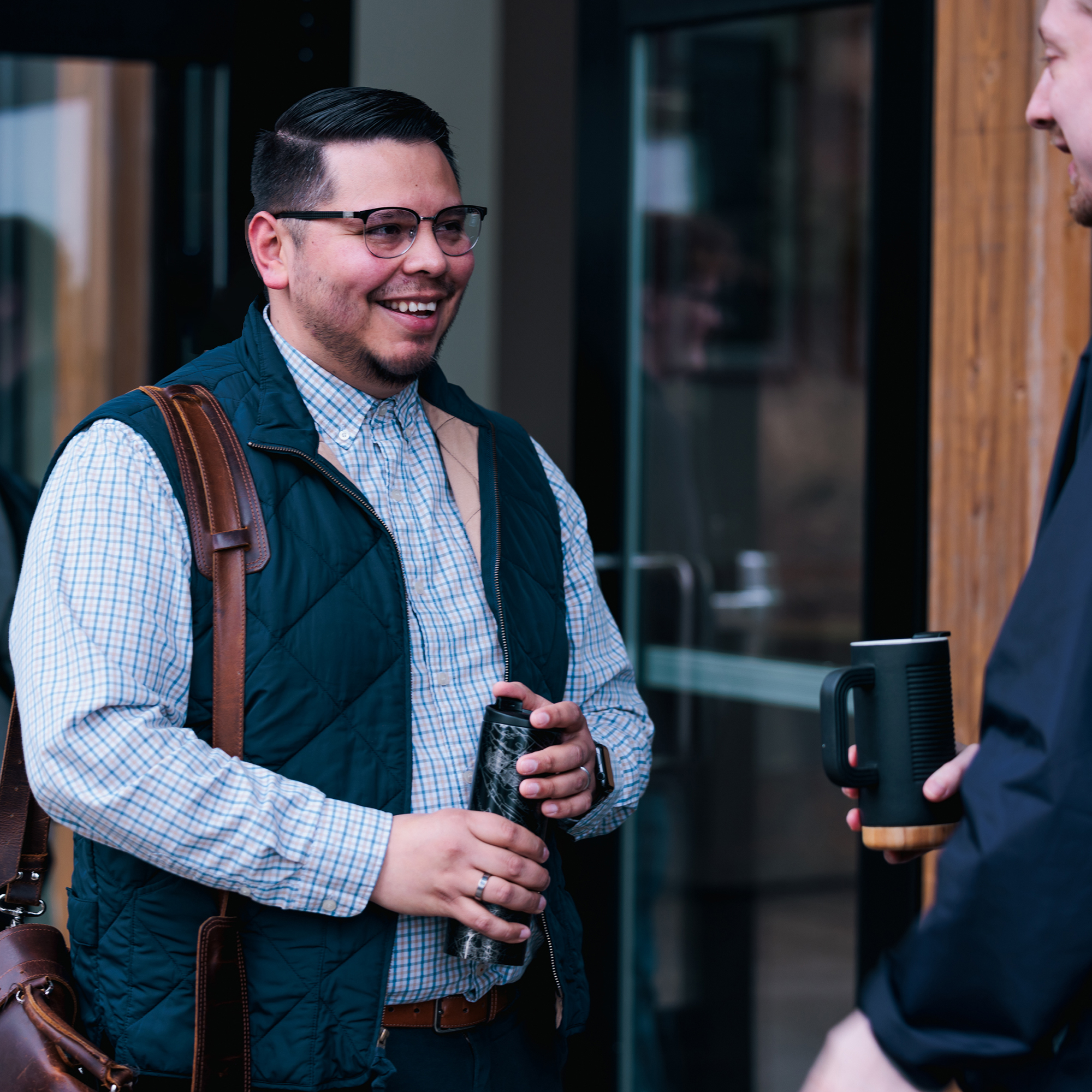 A graduate student carrying a brown leather bag over his shoulder, dressed casually in a light shirt and jeans.