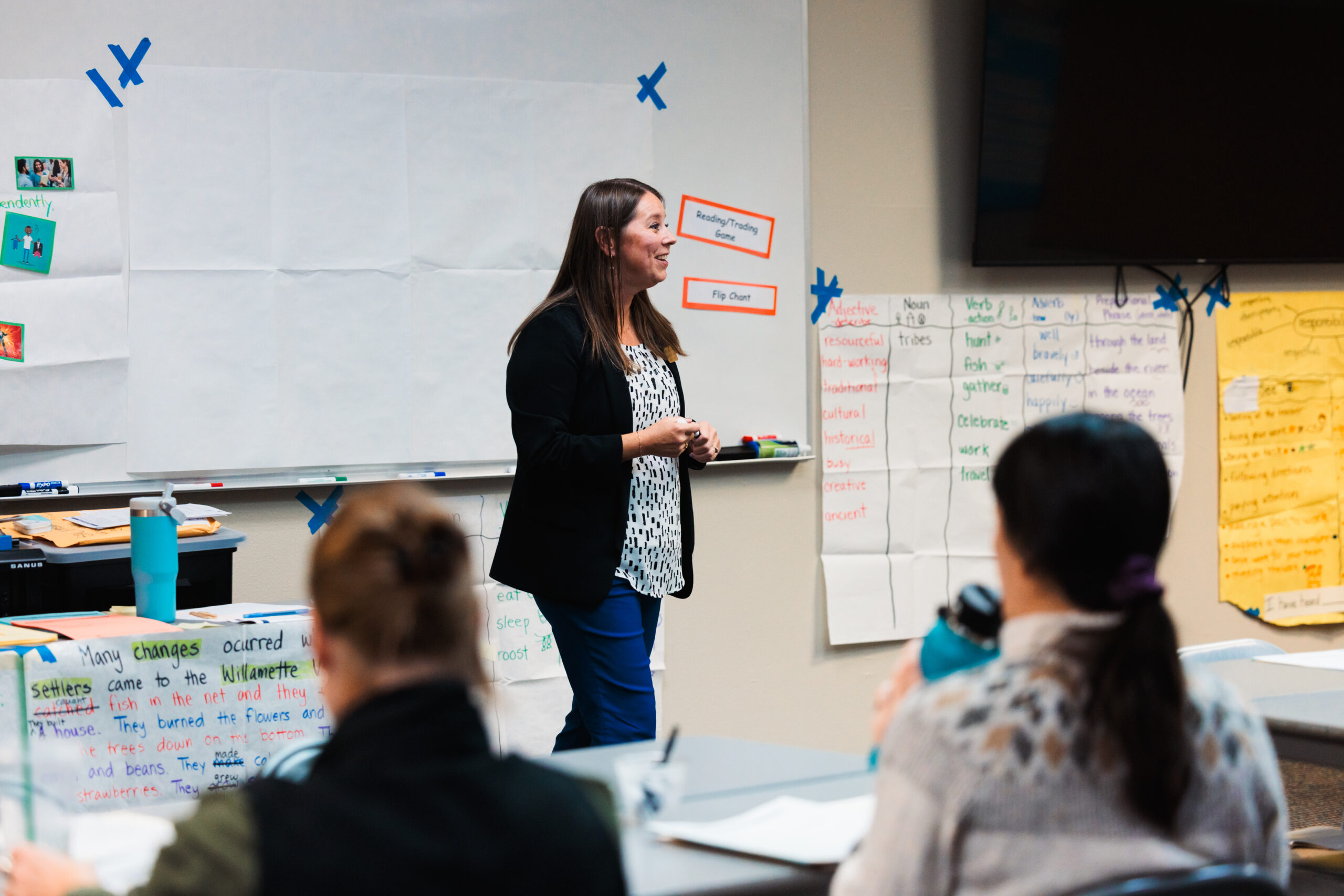 A woman is in front of a whiteboard, explaining a concept to the class.
