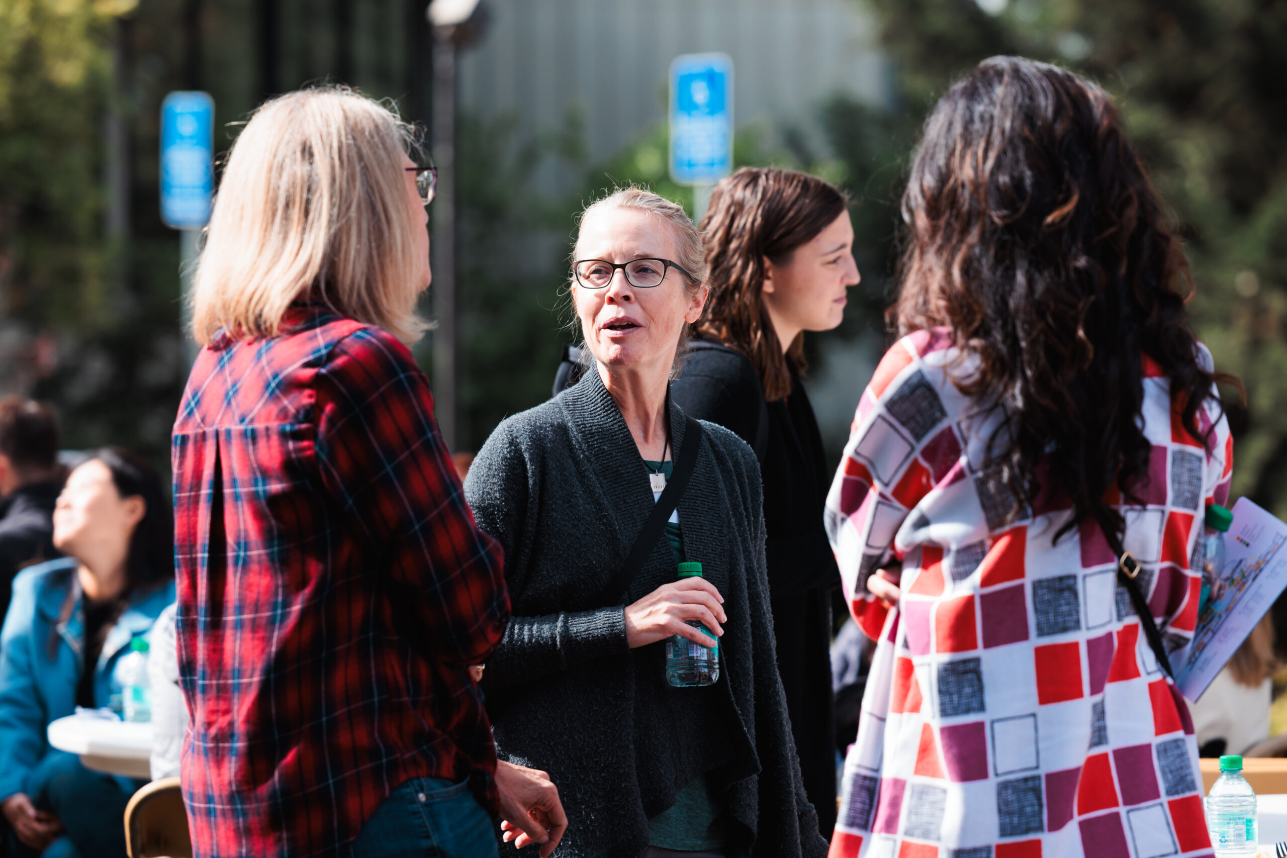 Three women conversing at an outdoor gathering, with a lively atmosphere.