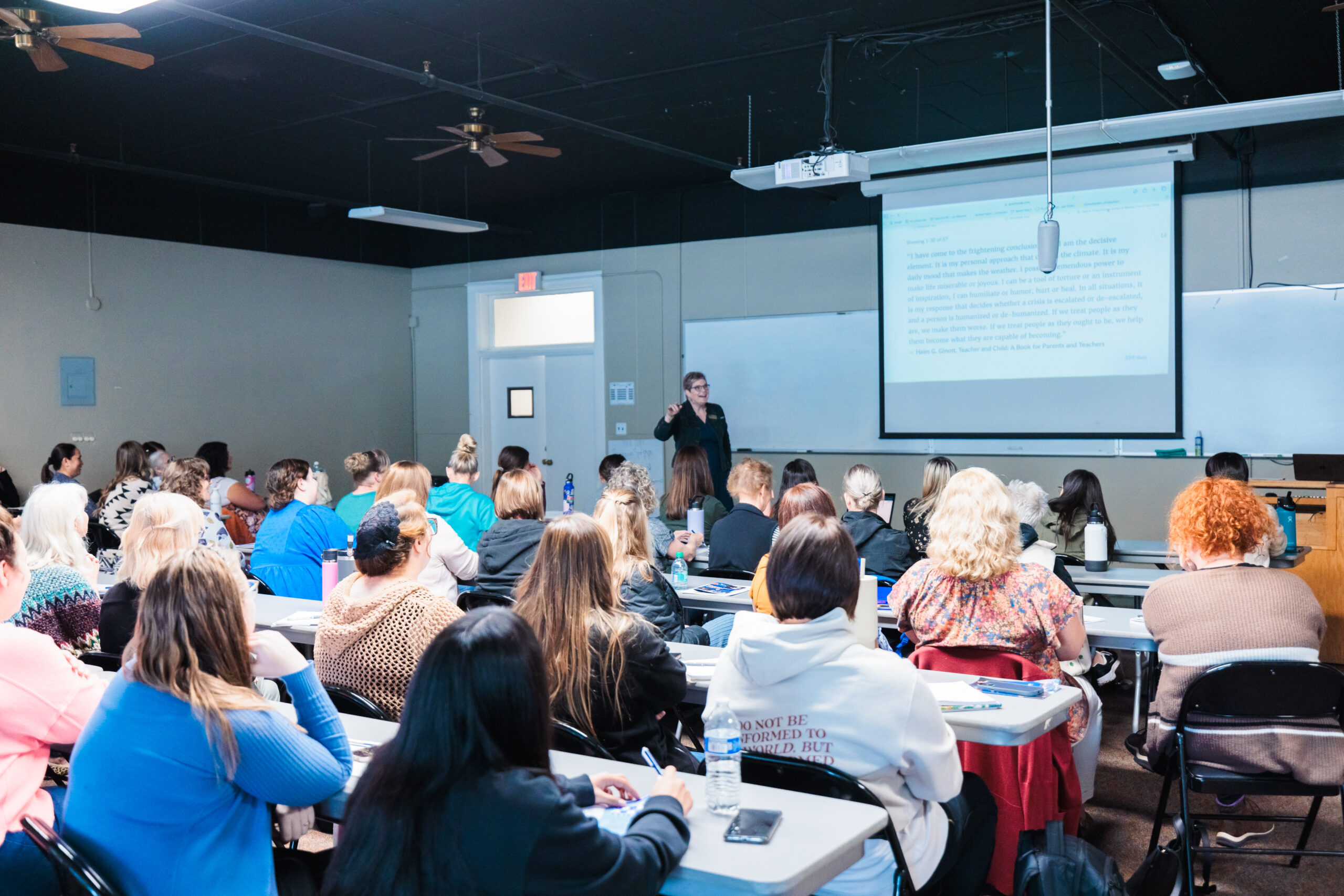 A woman stands before a group, delivering a presentation and interacting with her audience.