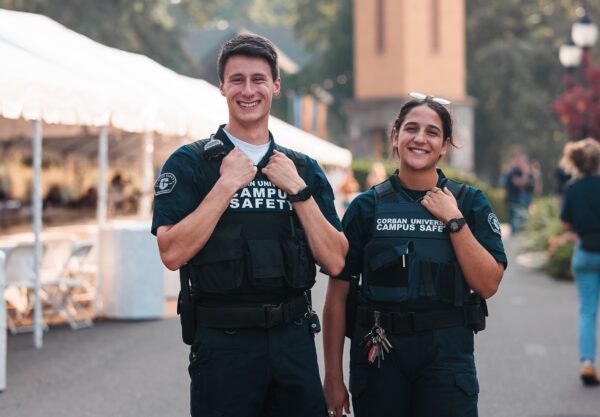 Two campus safety officers are positioned in front of tents, overseeing the surroundings for safety.