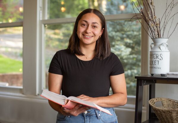 A woman smiles while holding a book in her hands, exuding joy and enthusiasm for reading.