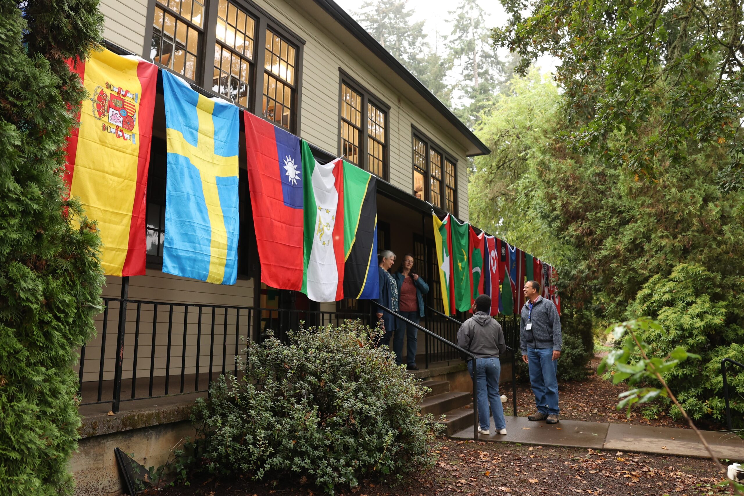 People standing together outside a building with many country flags, participating in World Outreach Week activities.