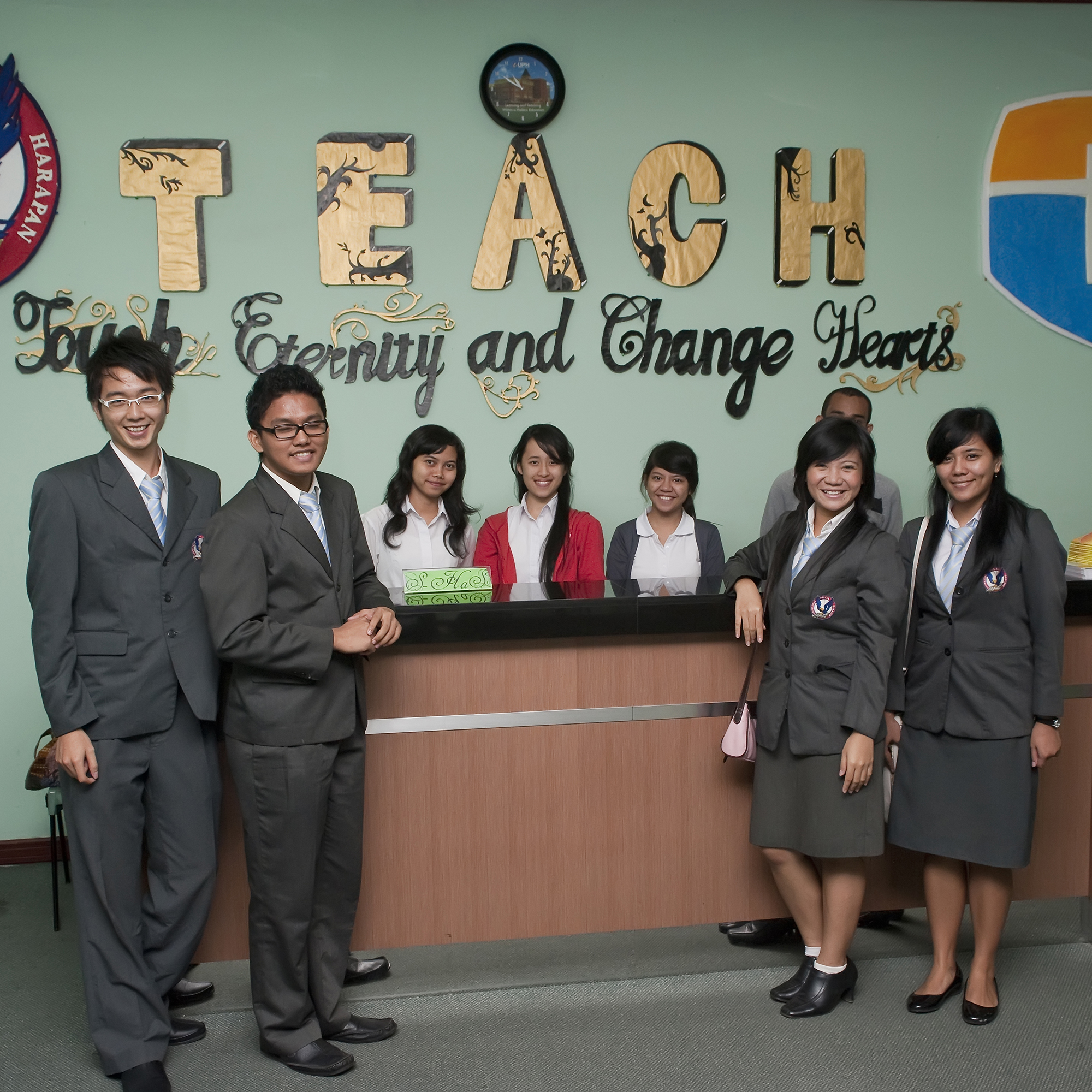 A group of teachers in training in Indonesia standing together, smiling in front of a sign that says "Teach."