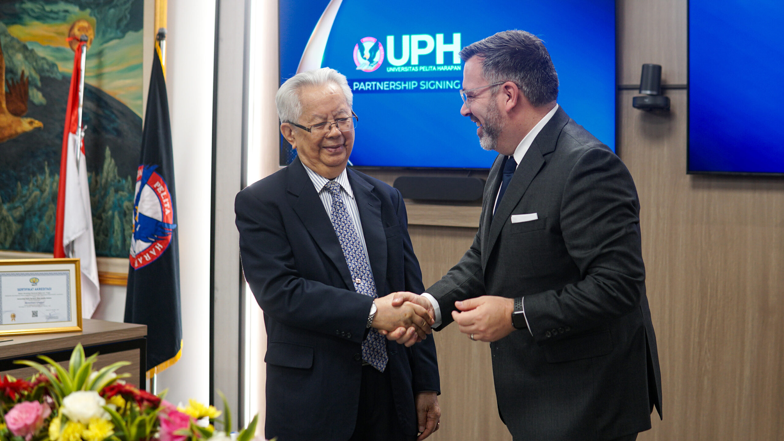 University leaders shake hands as they finalize a partnership agreement.