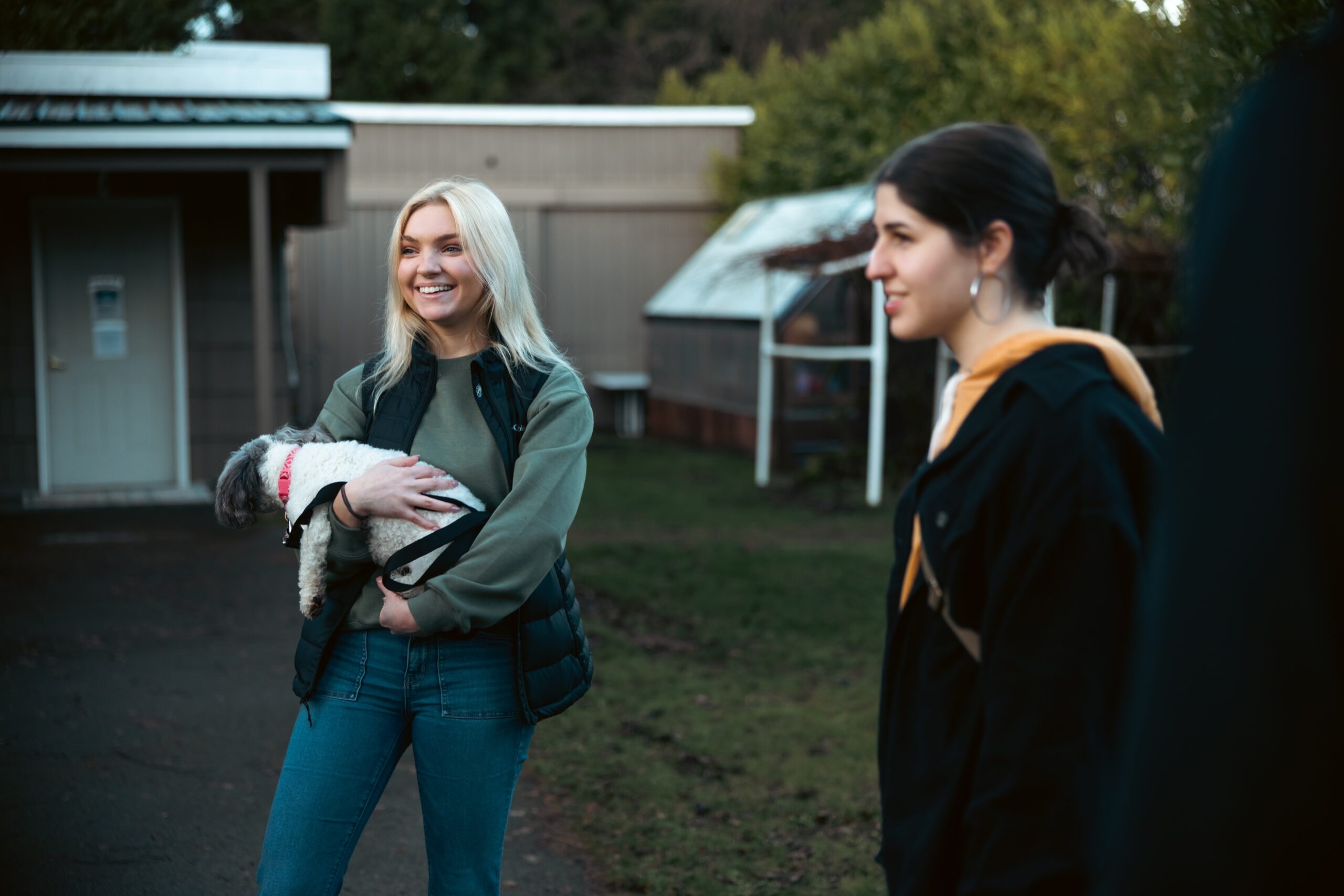 A woman stands holding a dog close to her chest, both appearing happy and engaged in the moment.