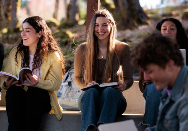 A diverse group of young people sitting together outside, engaged in conversation and enjoying each other's company.