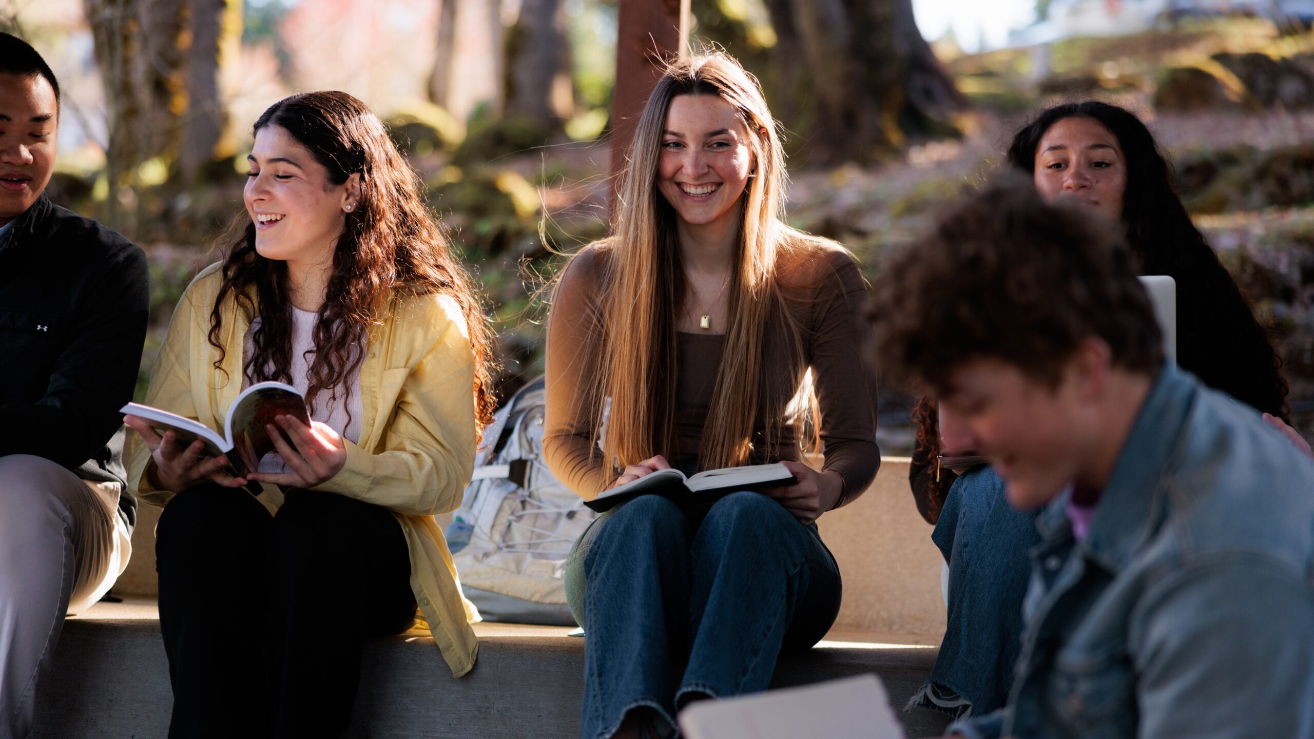 A diverse group of young people sitting together outside, engaged in conversation and enjoying each other's company.