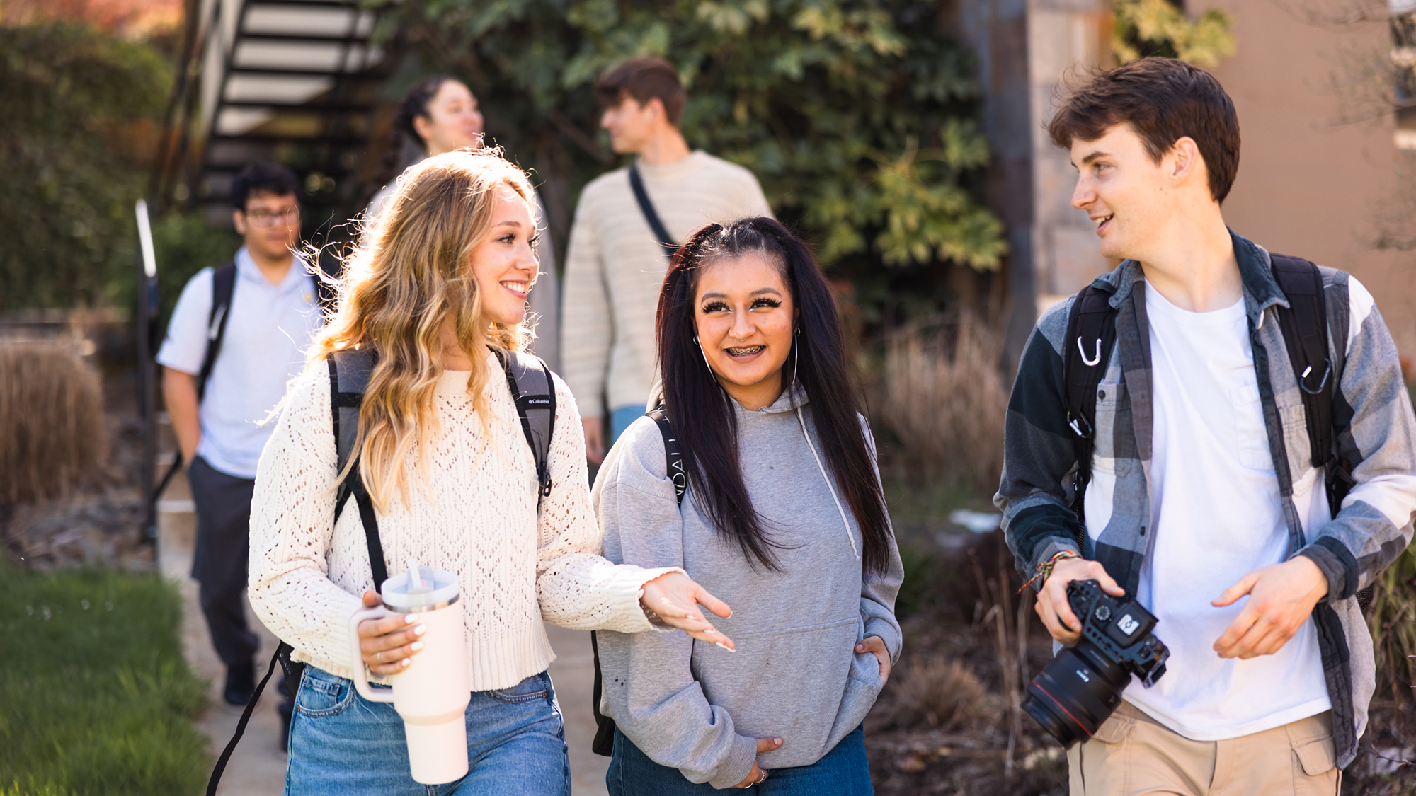 A group of students walking along a sidewalk, casually chatting and sharing laughter as they move together.