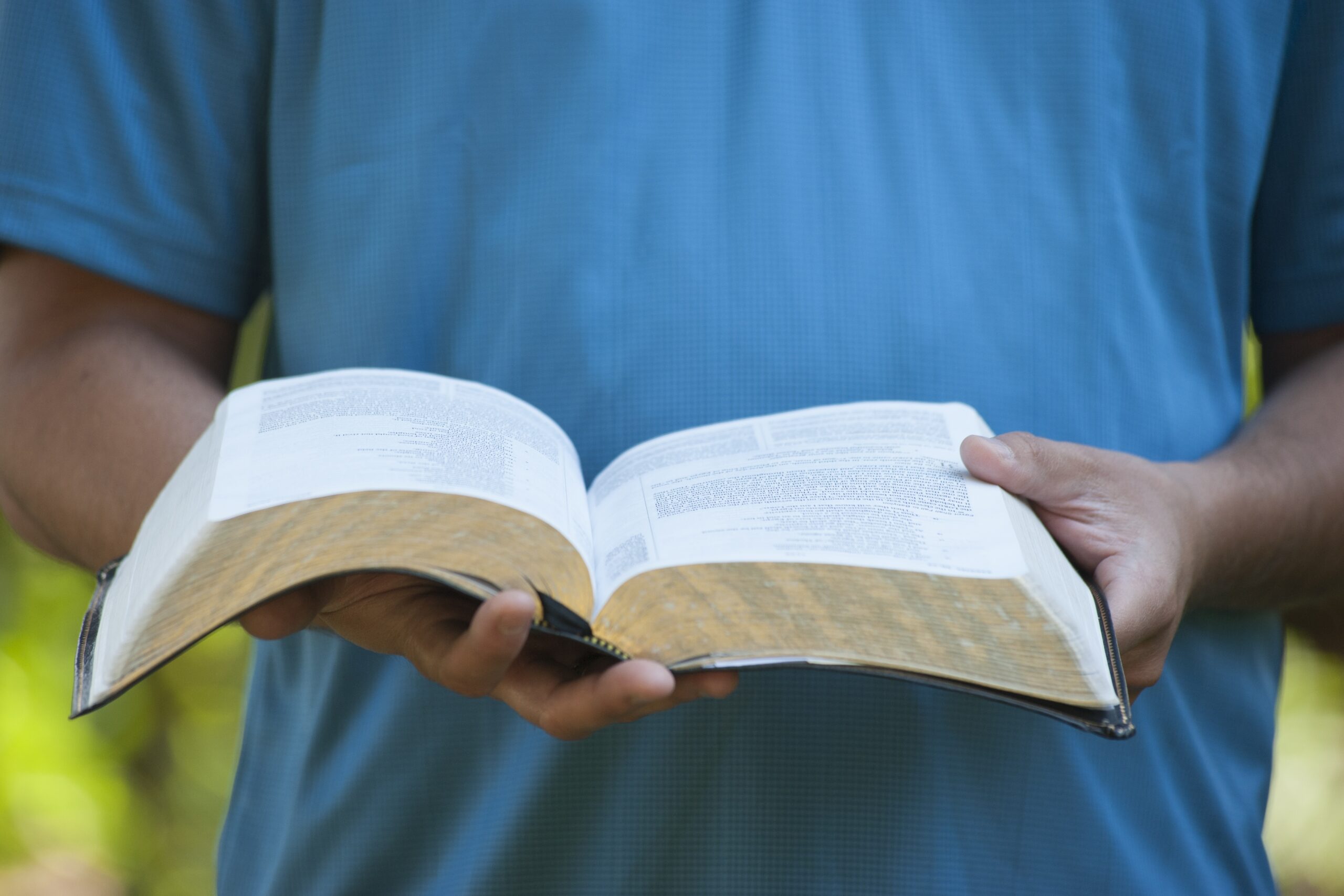 A man grasping an open Bible, looking down at the pages, conveying a sense of contemplation and reverence.