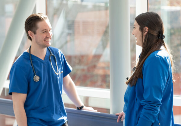 Two nurses, one male and one female, conversing with each other in a healthcare environment.