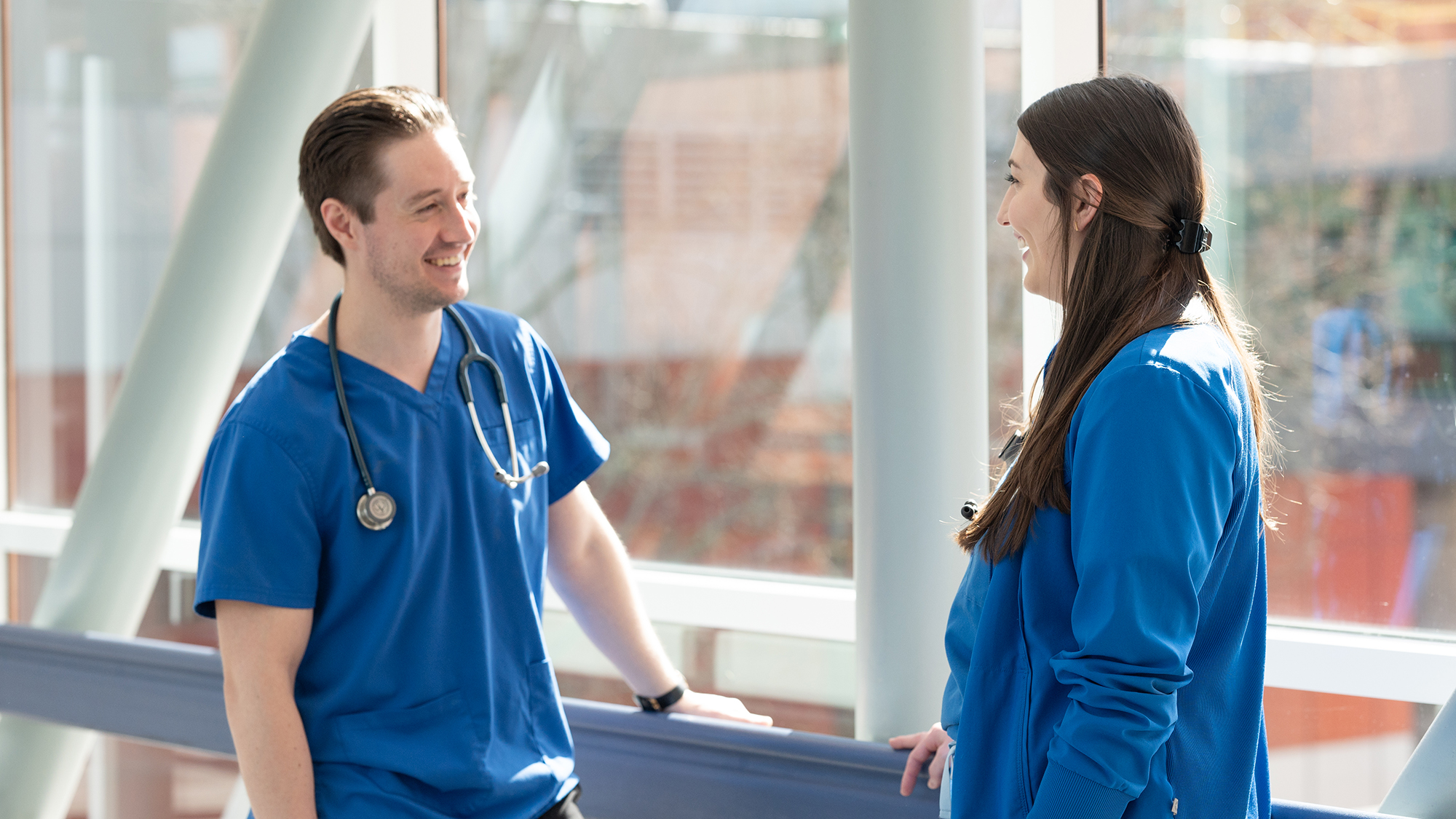 Two nurses, one male and one female, conversing with each other in a healthcare environment.