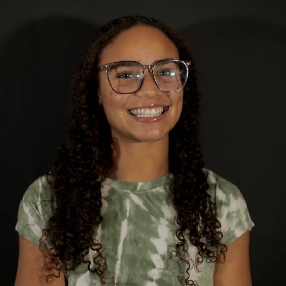 Portrait of Jessica McMillian, a young woman with glasses in a green tie-dye shirt.