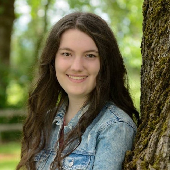 Portrait of Kayla Moore, a young woman against the backdrop of trees.