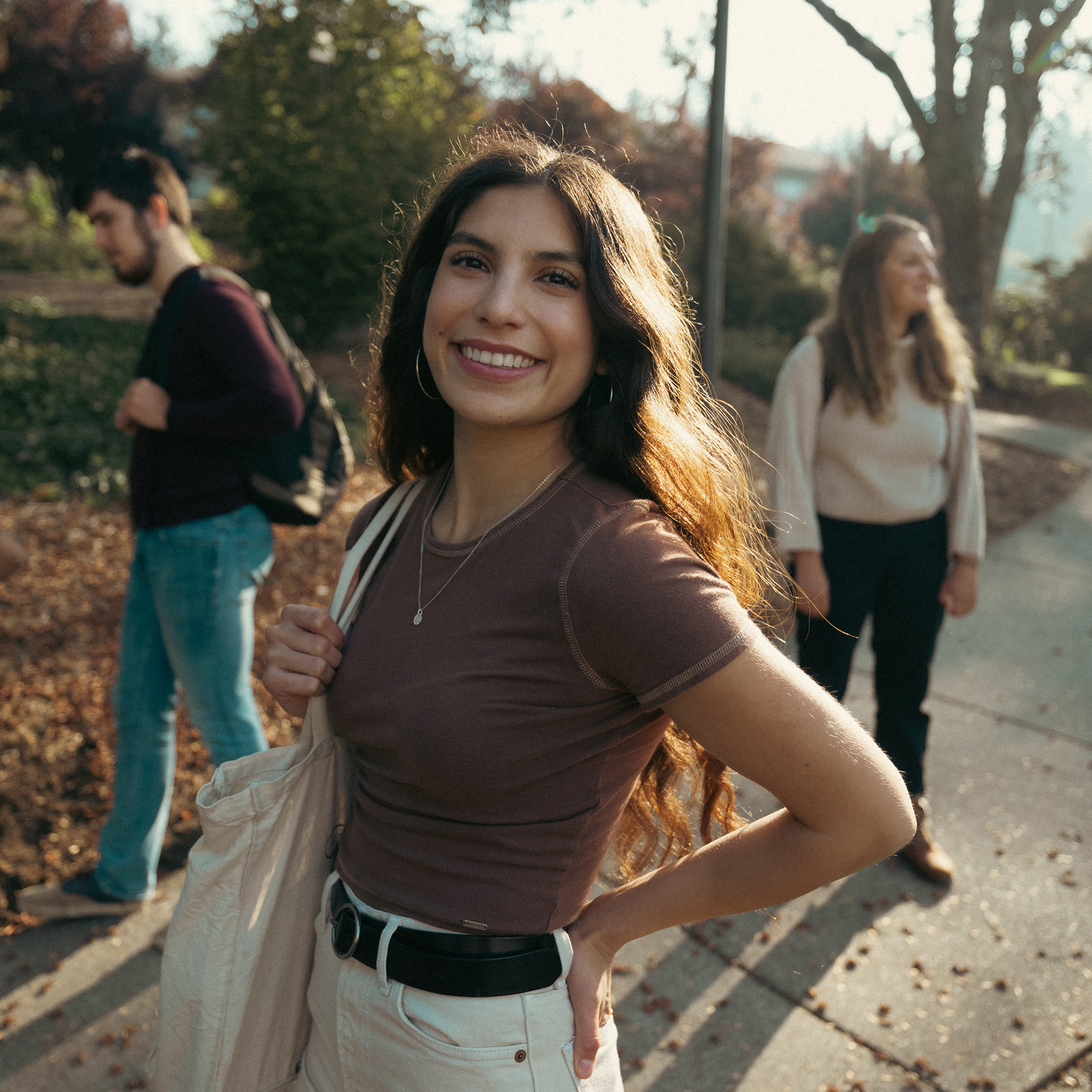 A smiling woman walks with her friends, enjoying a sunny day together on campus.