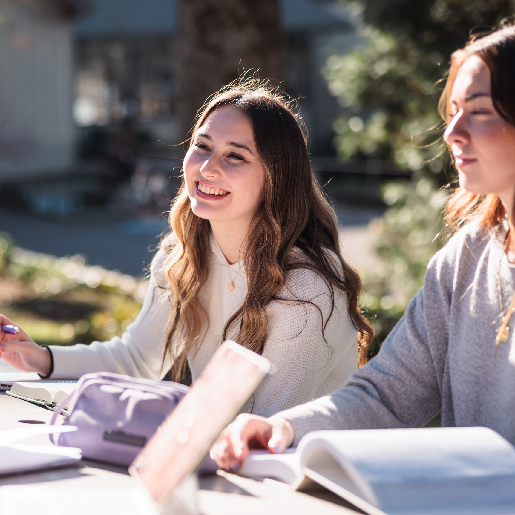 A female college student studies outside in the sunshine at a picnic table with other students.