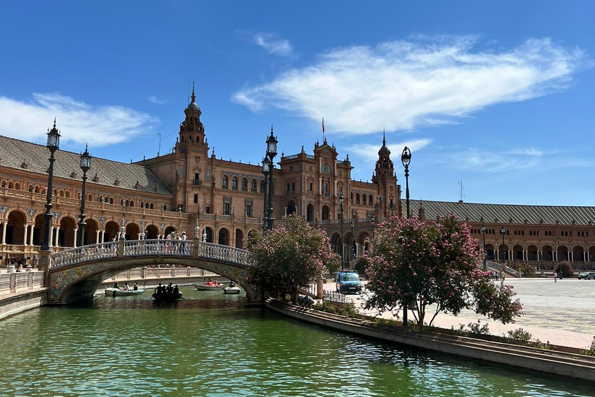 A serene river flows through Plaza de España in Seville, Spain, surrounded by beautiful architecture and lush greenery
