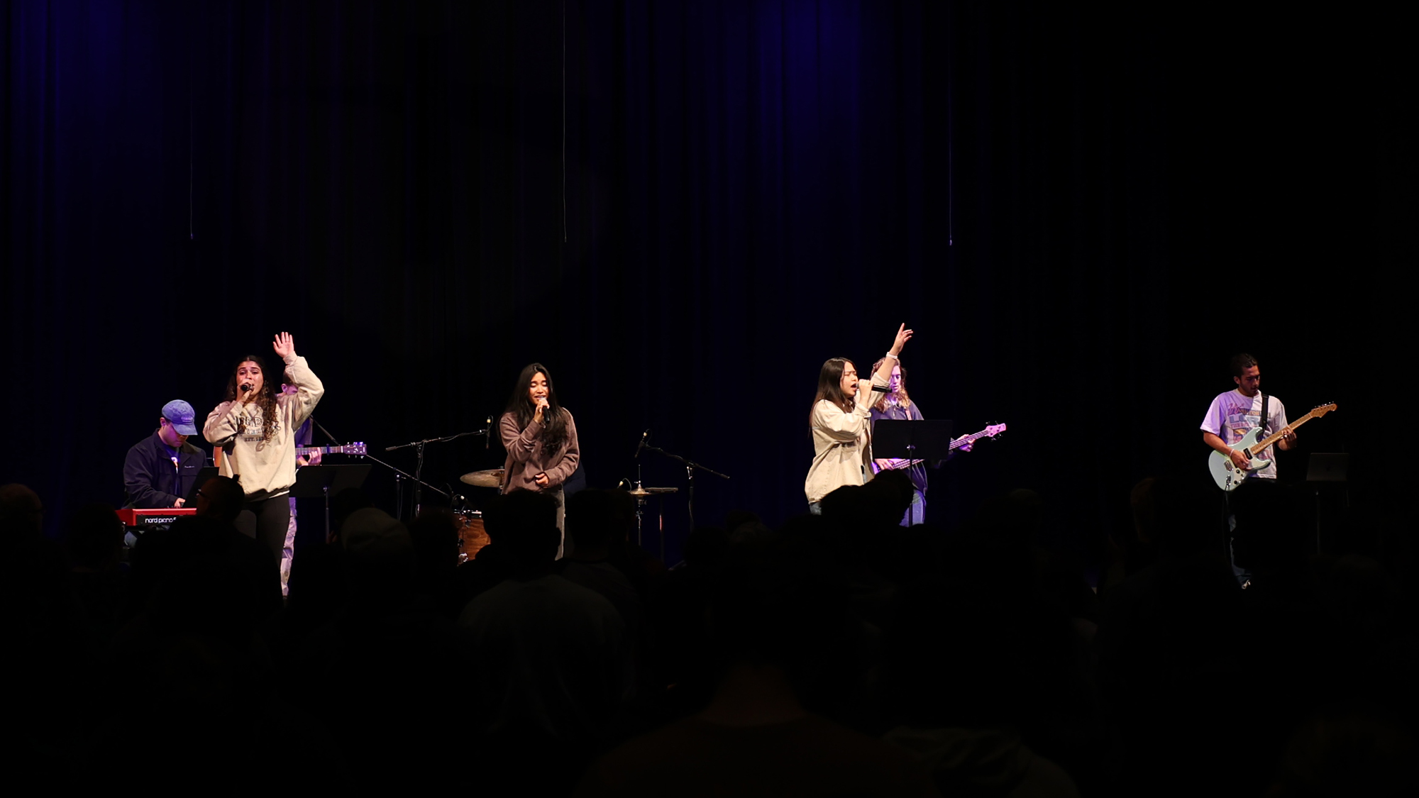 A group of students on stage leading worship during chapel, raising their hands in praise.