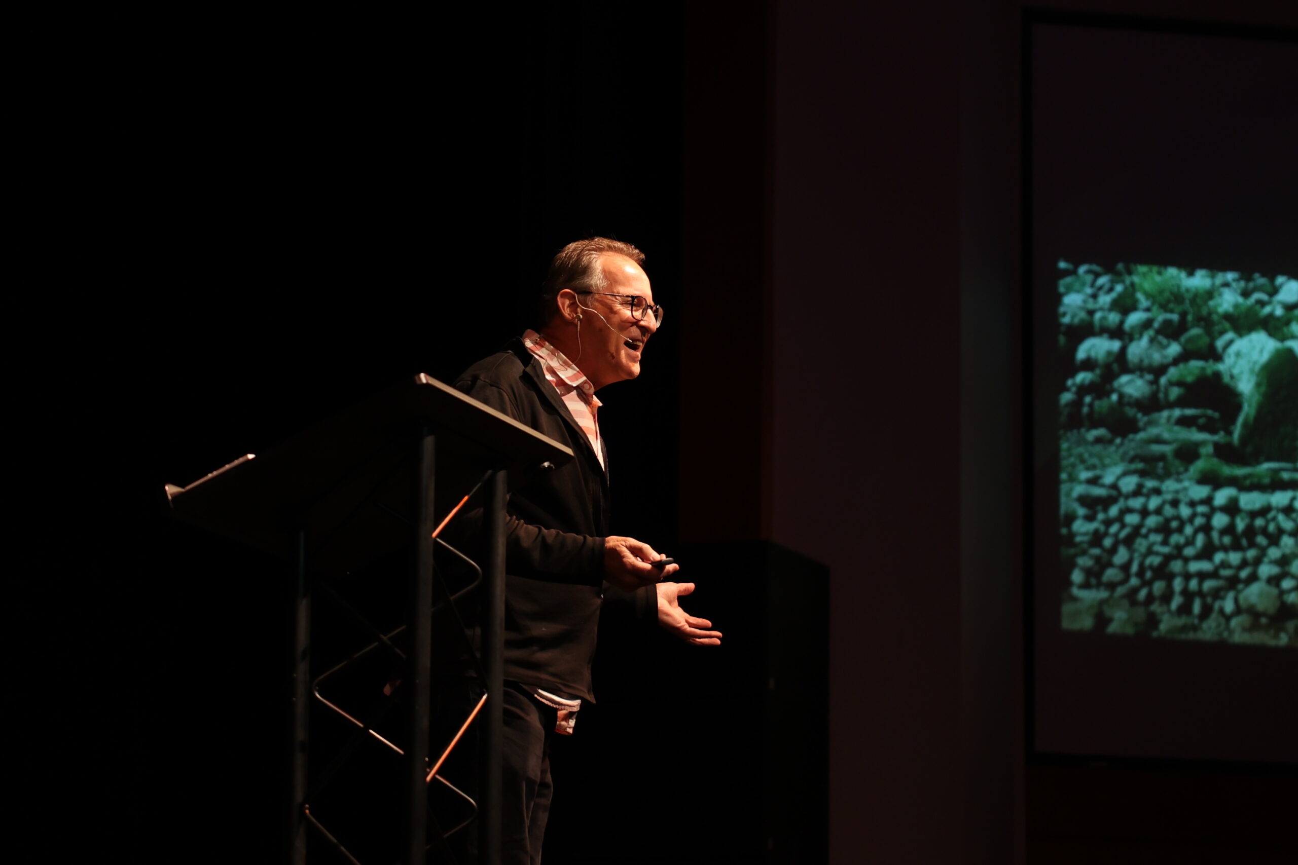 A man stands at a podium, addressing an audience with a presentation screen behind him for chapel.
