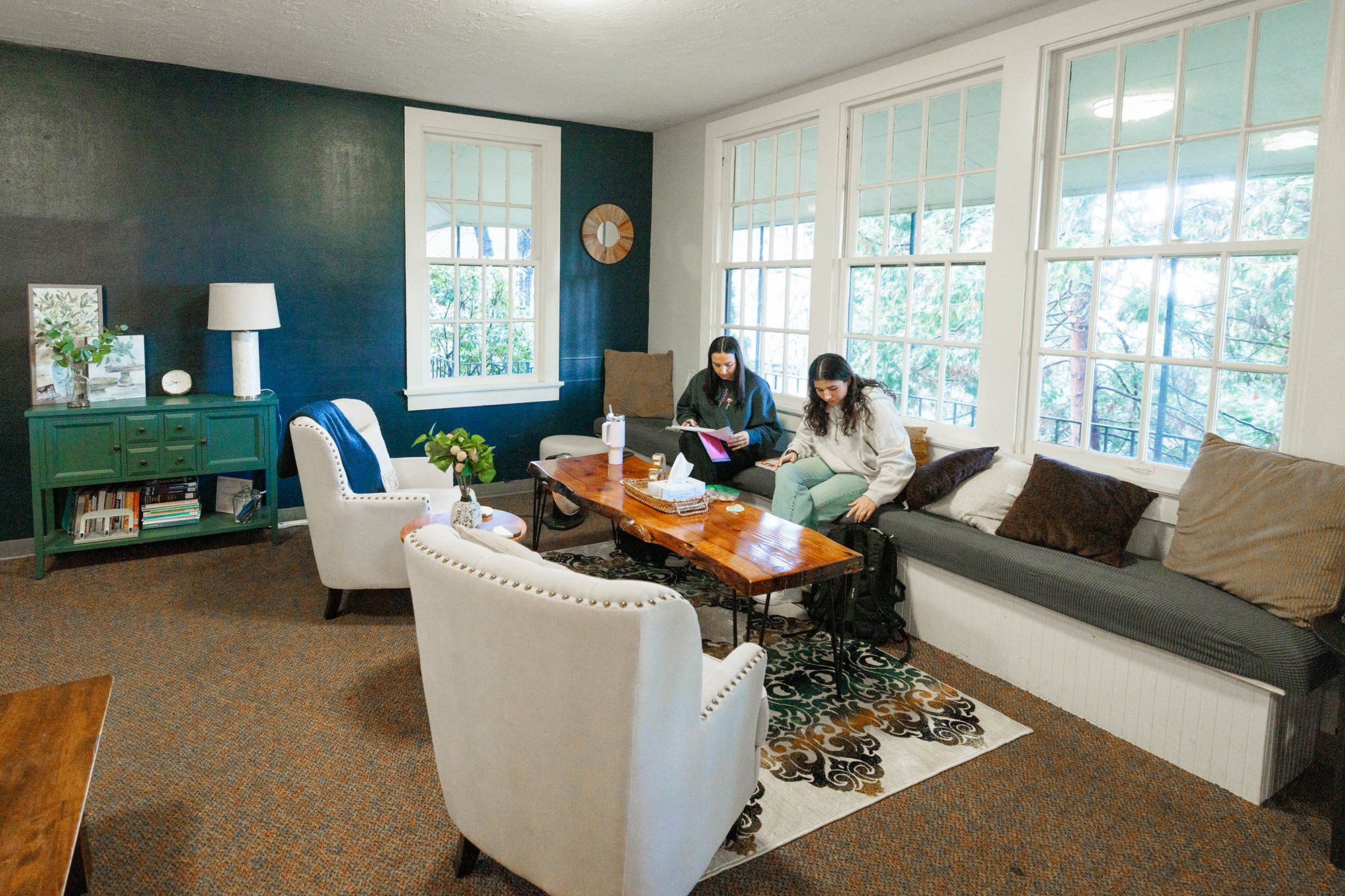 Two women relax in the commuter lounge, sitting together in a bright room with large windows.