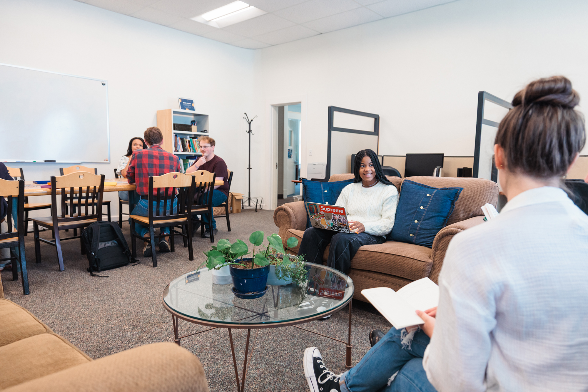 Students sitting around a table and on couches in the study room, sharing ideas in a comfortable setting.