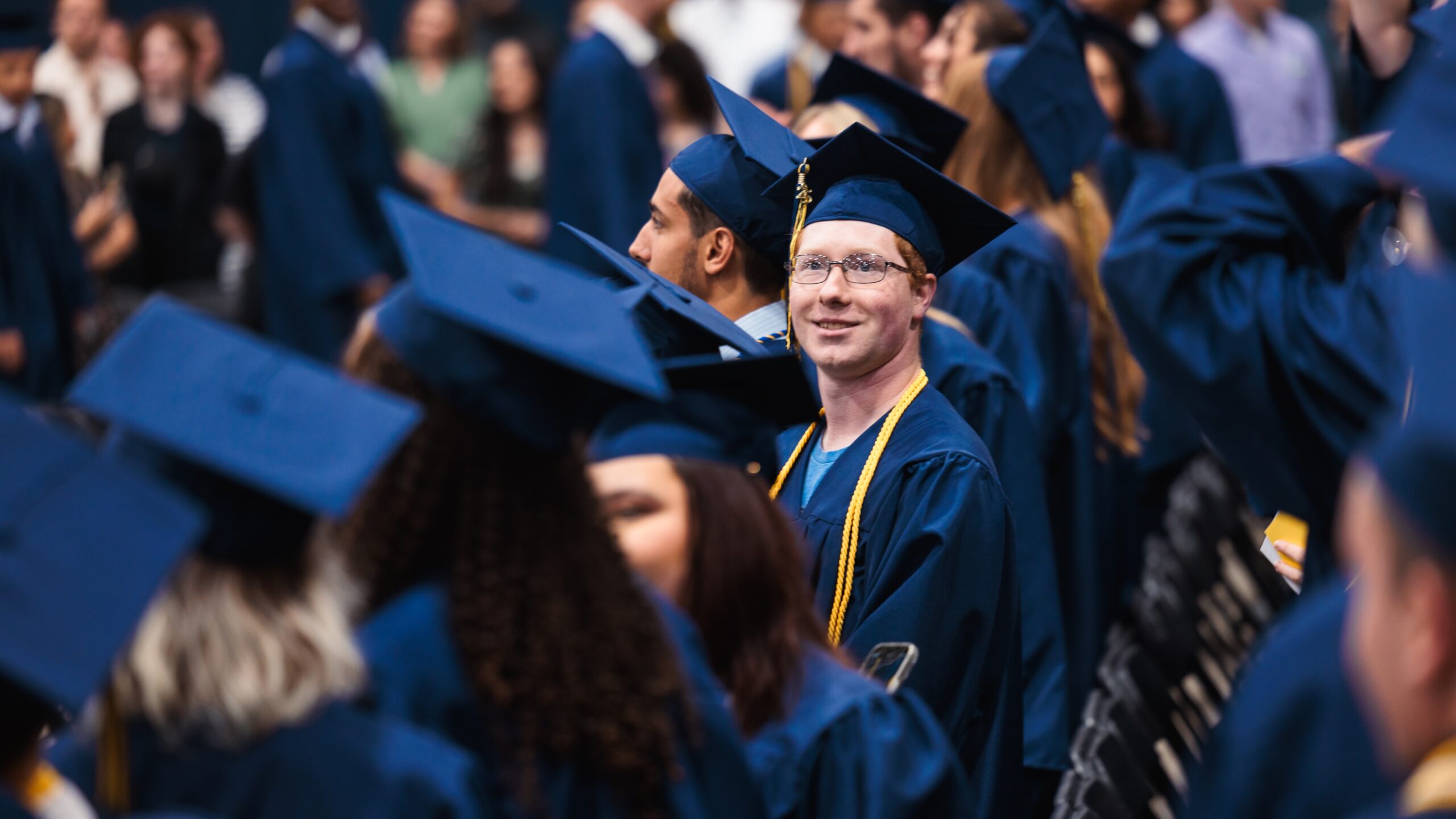 A diverse group of graduates in blue gowns and caps proudly stand together at their commencement ceremony.