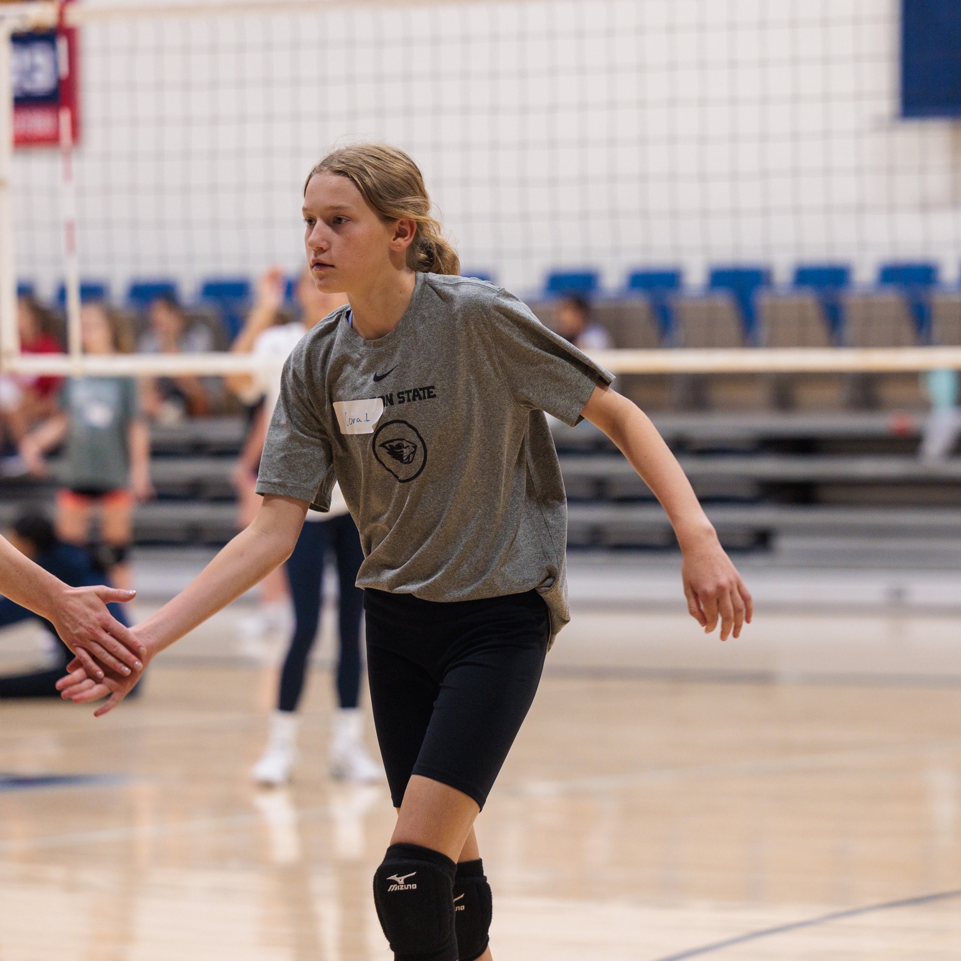 Girl wearing black knee pads gives a high five in a gym.