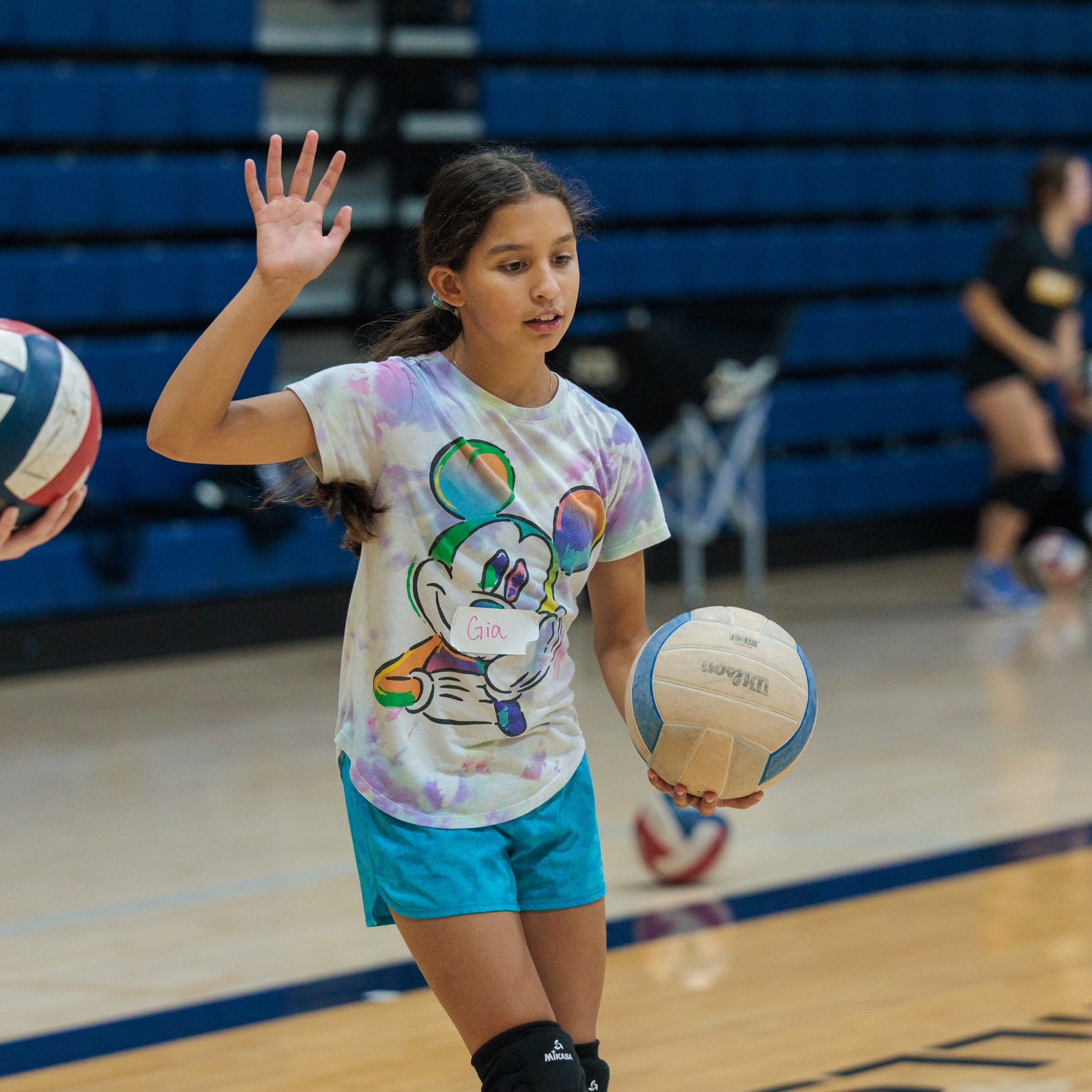 A young girl stands confidently, gripping a volleyball in her hands and practicing her serve.