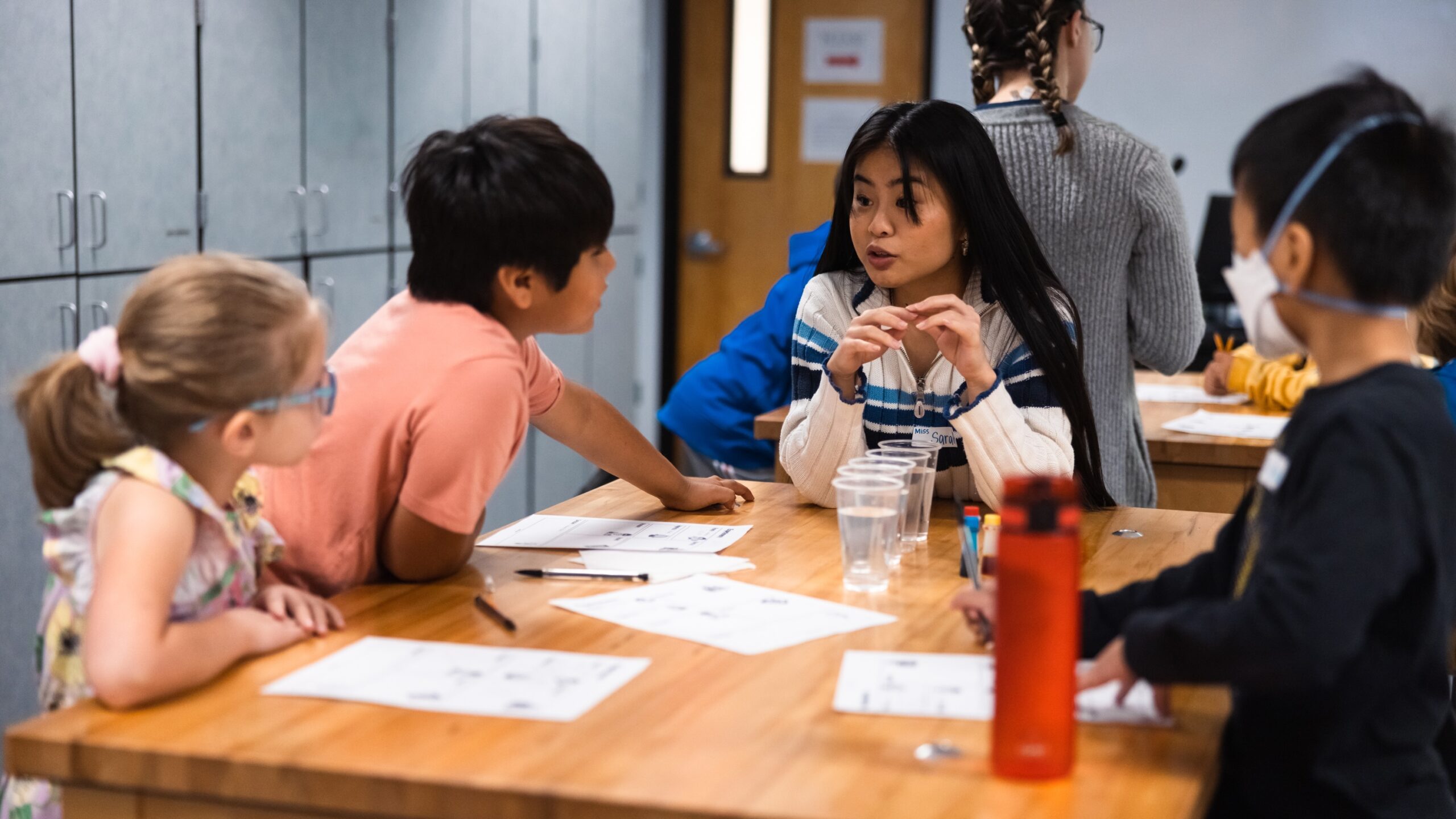 A group of children sitting around a table in a classroom, engaged in an activity together for Science Saturday.