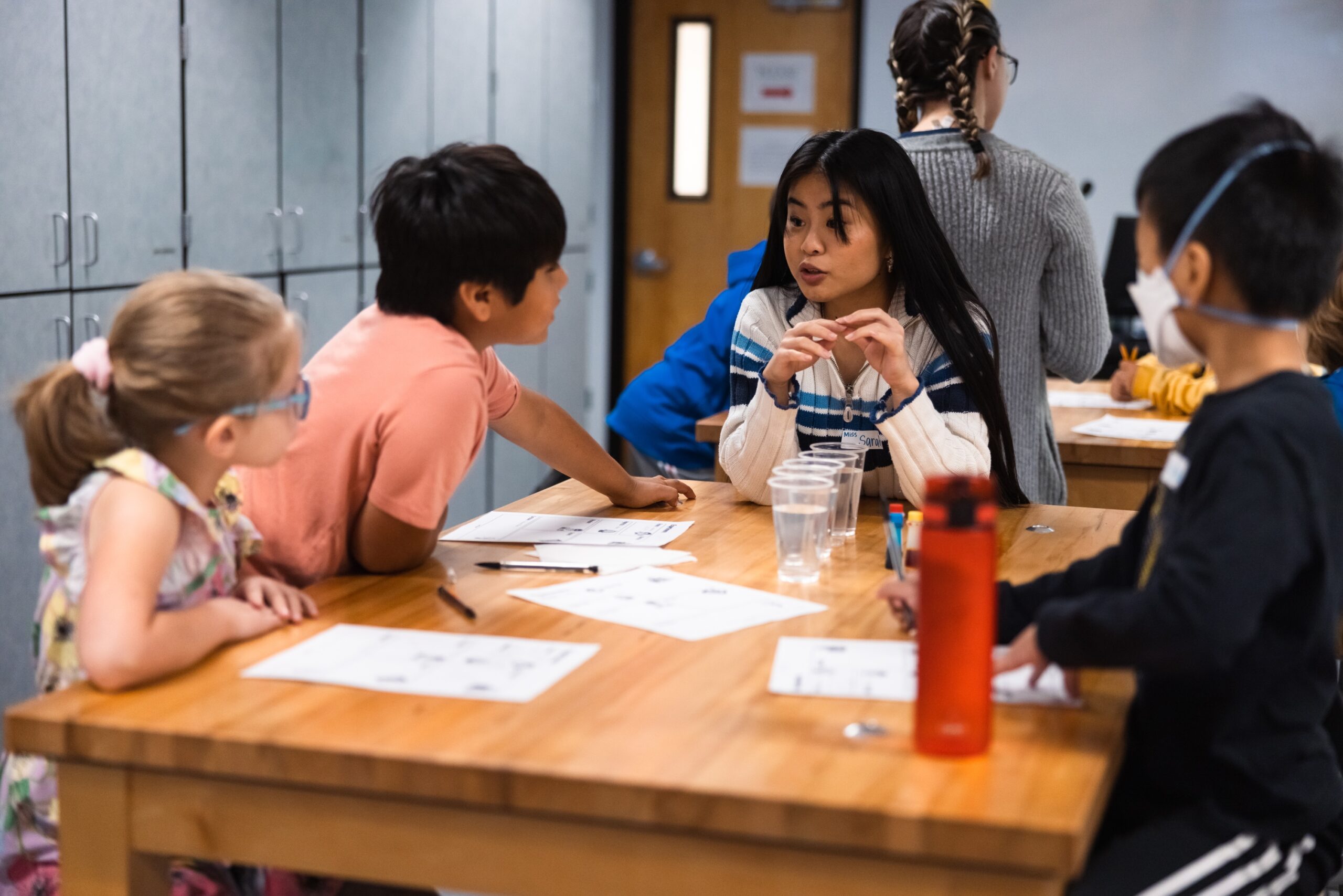 A group of children sitting around a table in a classroom, engaged in an activity together for Science Saturday.