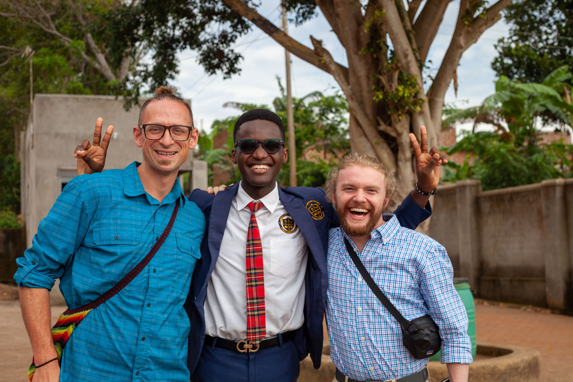 A faculty member and a student pose for a photo with a local man in Uganda, all smiling happily.