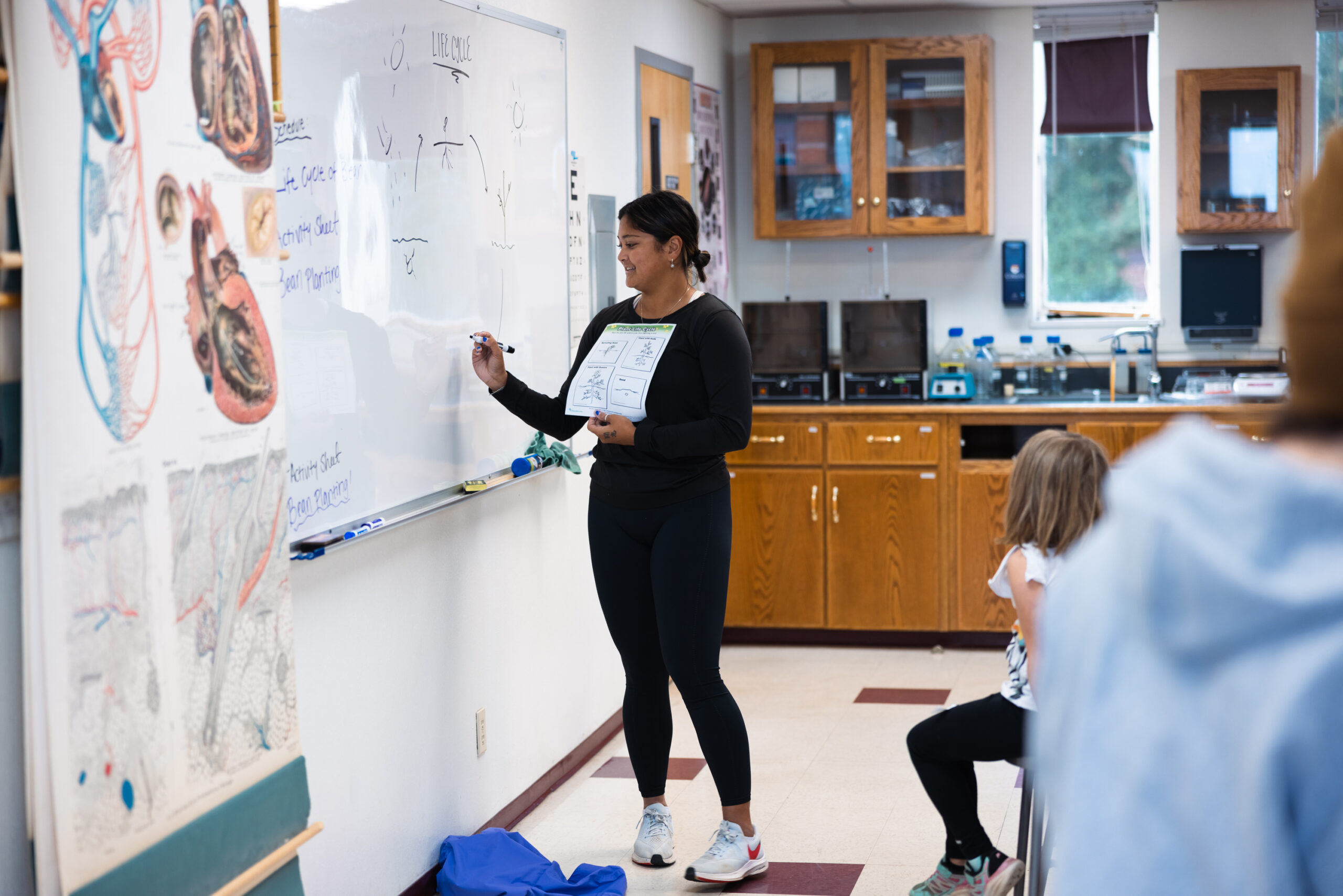 A female teacher instructs students in a classroom, engaging them with visual aids and interactive learning materials.