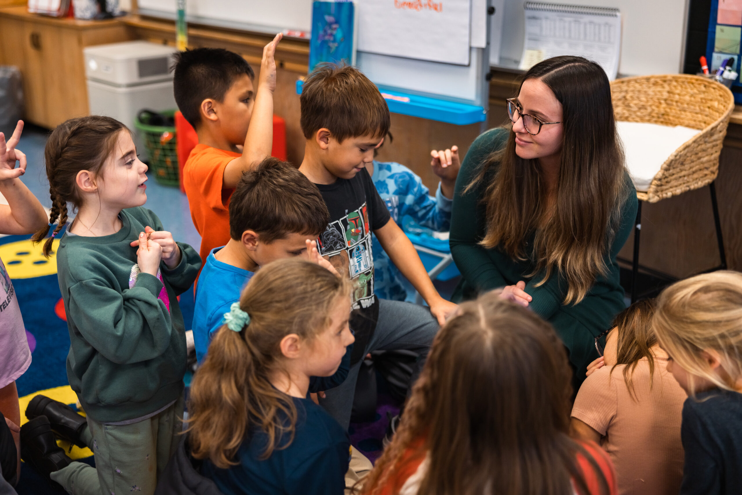 A teacher engages with a group of attentive children during a classroom discussion.