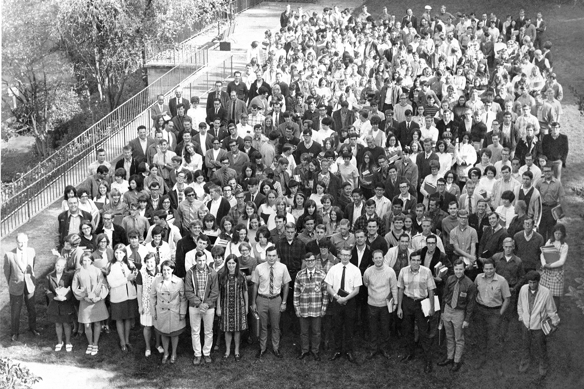 A large group of students from the 1970s standing together in a field, smiling and posing for a photograph.