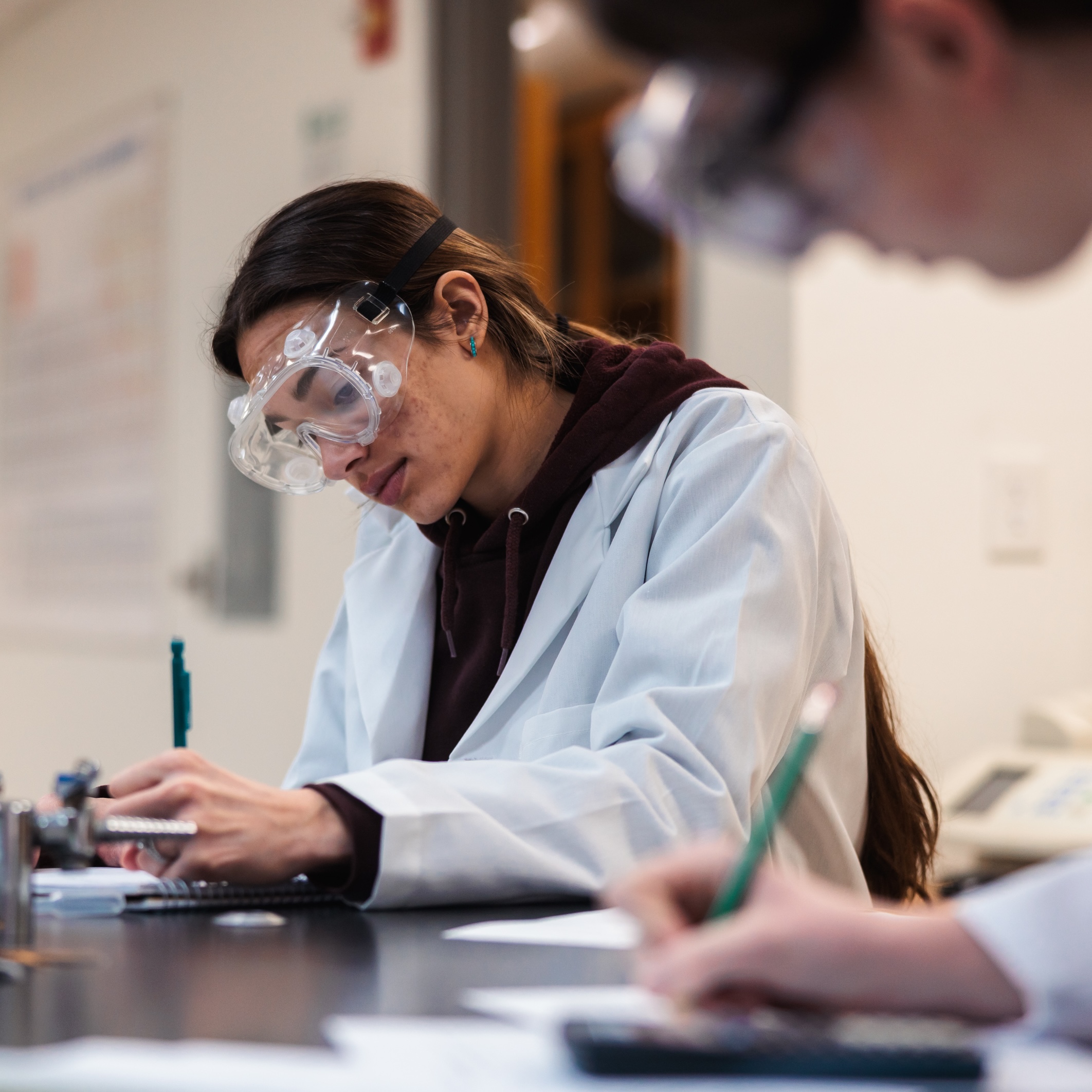 Two women in lab coats working on a project, focused on writing and analyzing data.
