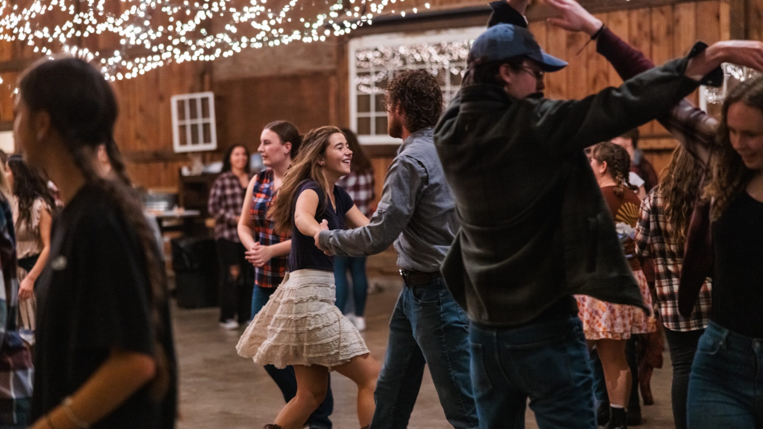 Students joyfully dancing in a barn illuminated by colorful lights and charming string lights for Harvestifall.