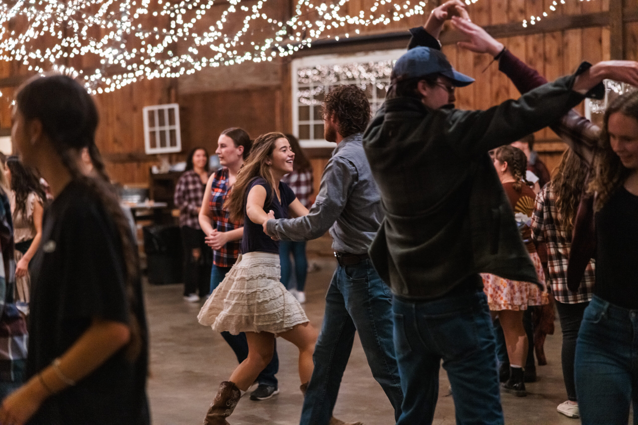 Students joyfully dancing in a barn illuminated by colorful lights and charming string lights for Harvestifall.