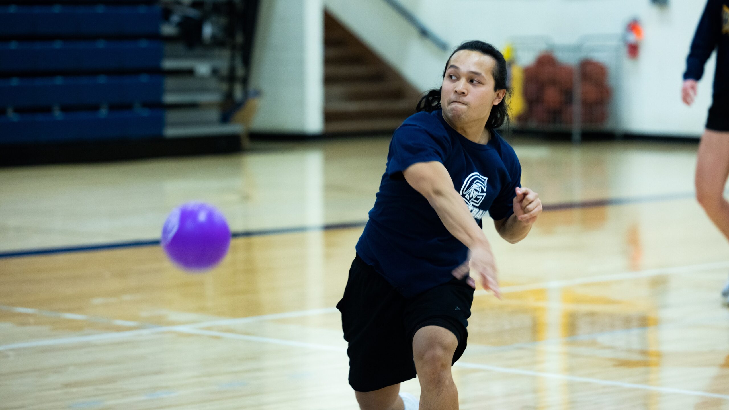 A man energetically throws a ball during an intramural dodgeball match in a gym.
