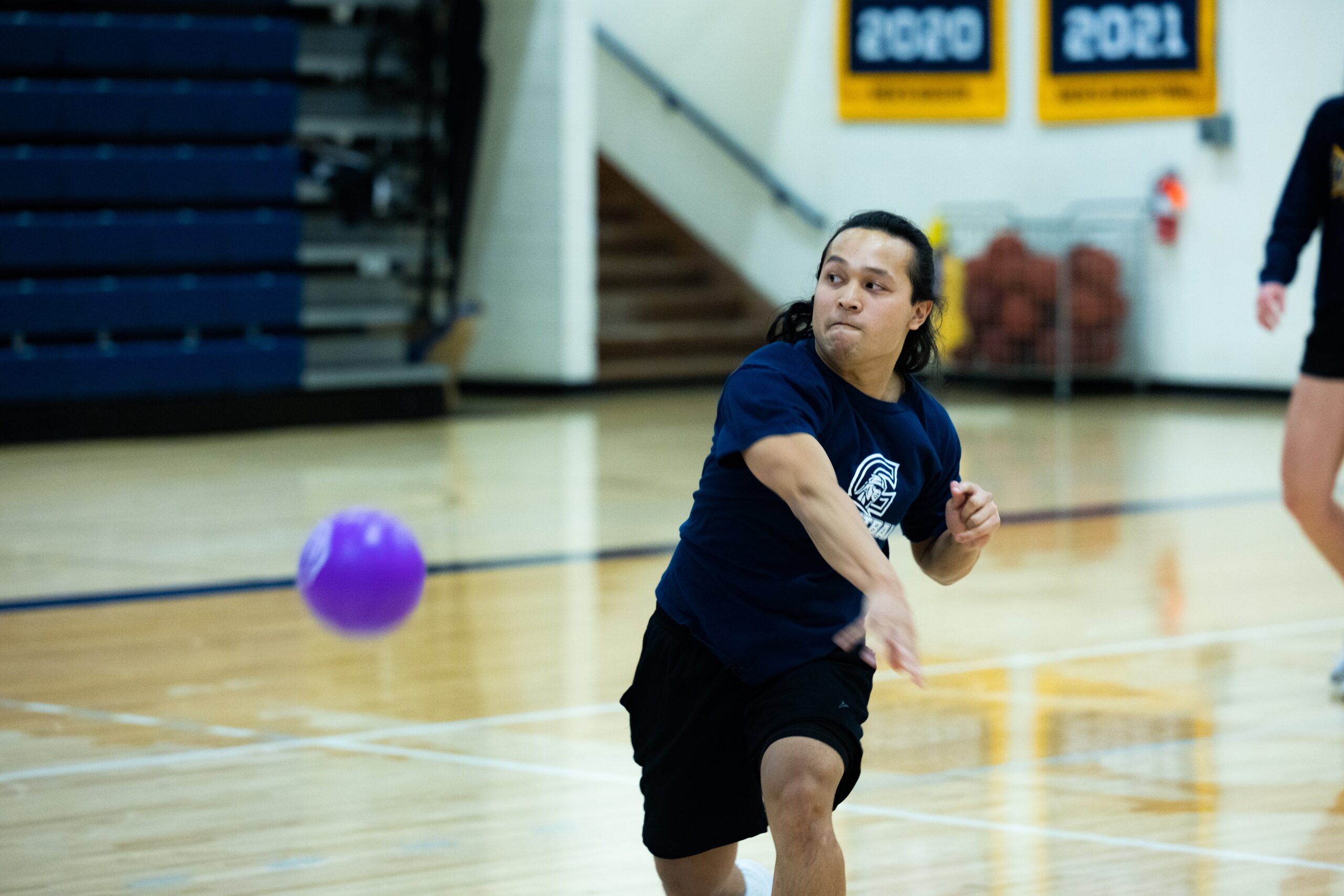A man energetically throws a ball during an intramural dodgeball match in a gym.