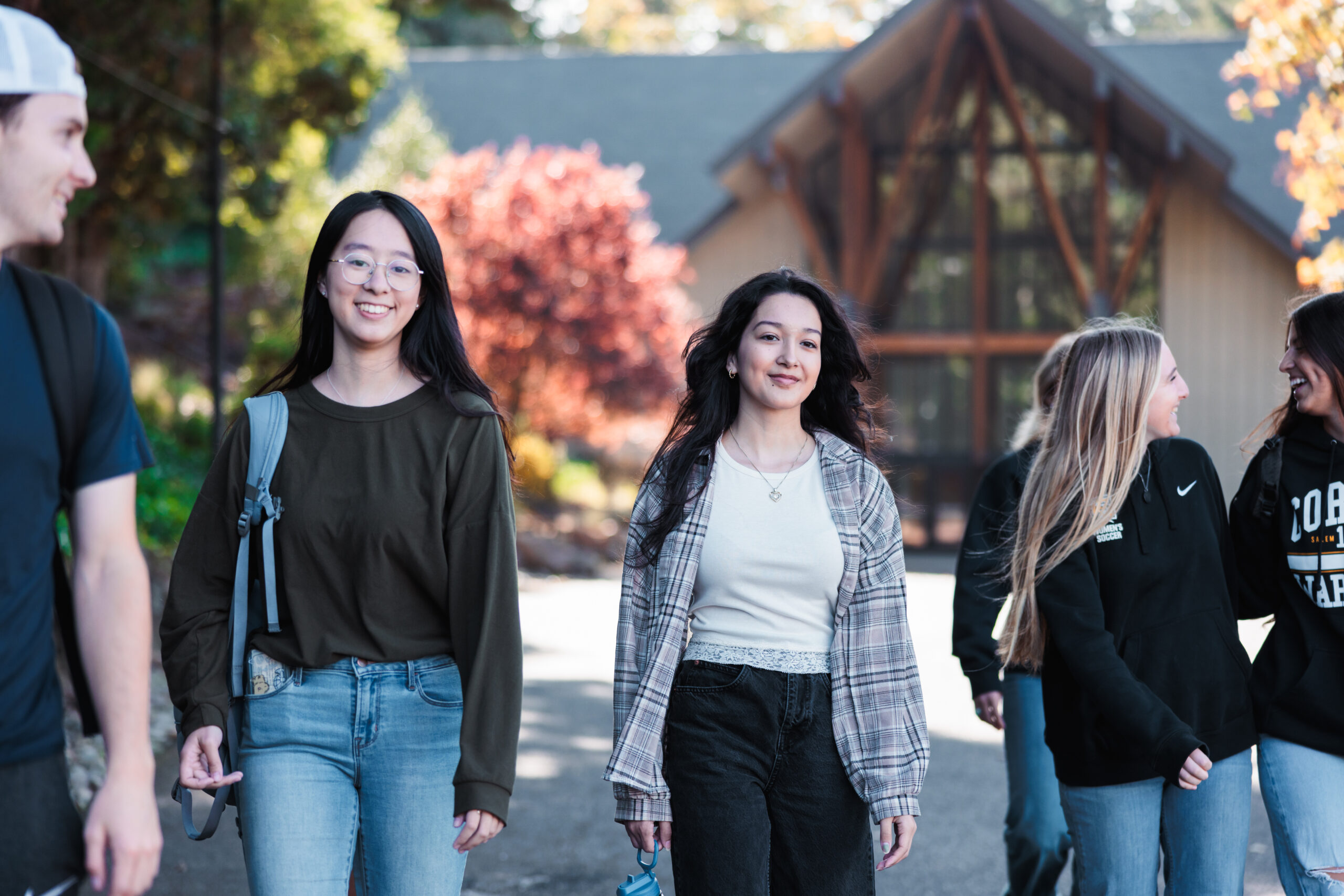 A diverse group of students walks side by side on a sidewalk, carrying backpacks and sharing smiles.