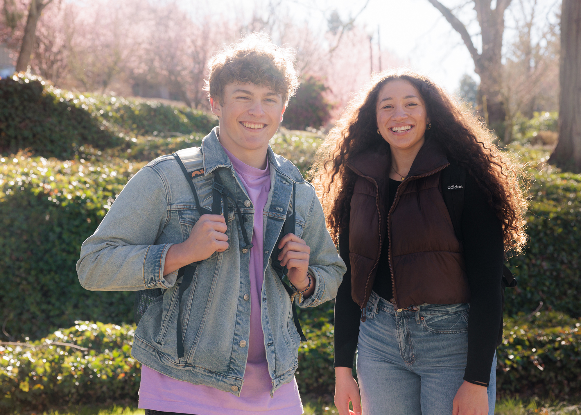 Two students stand smiling on Corban's campus, surrounded by nature and sunshine.