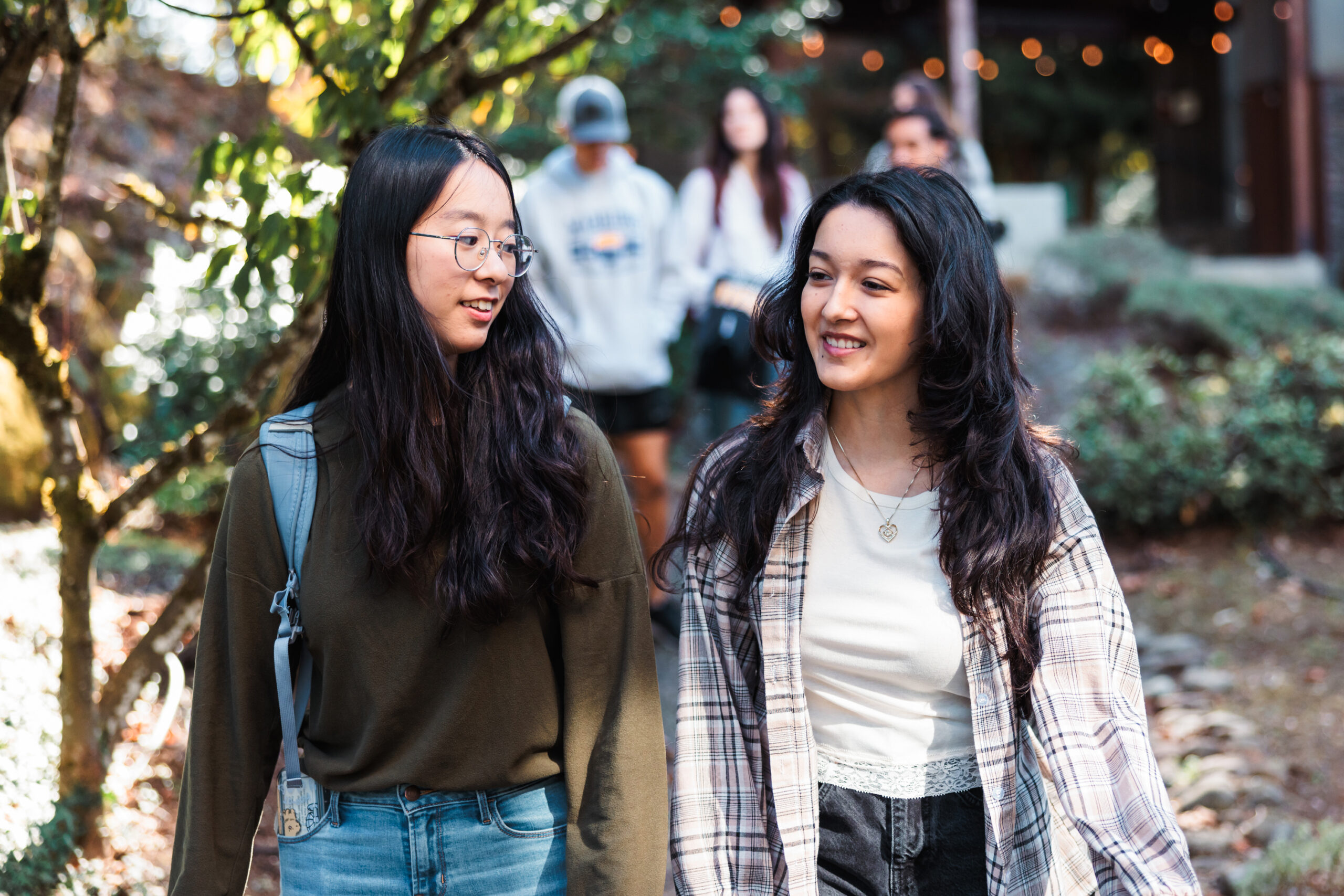 Two young women walk together along a path, chatting and enjoying a sunny day outdoors.