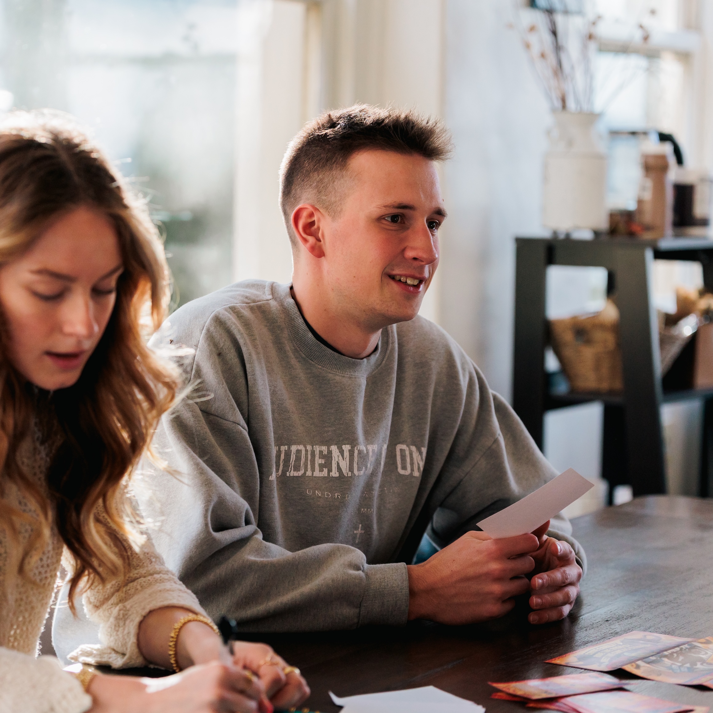 A young man and woman sit at a table, engaged in writing and discussion.