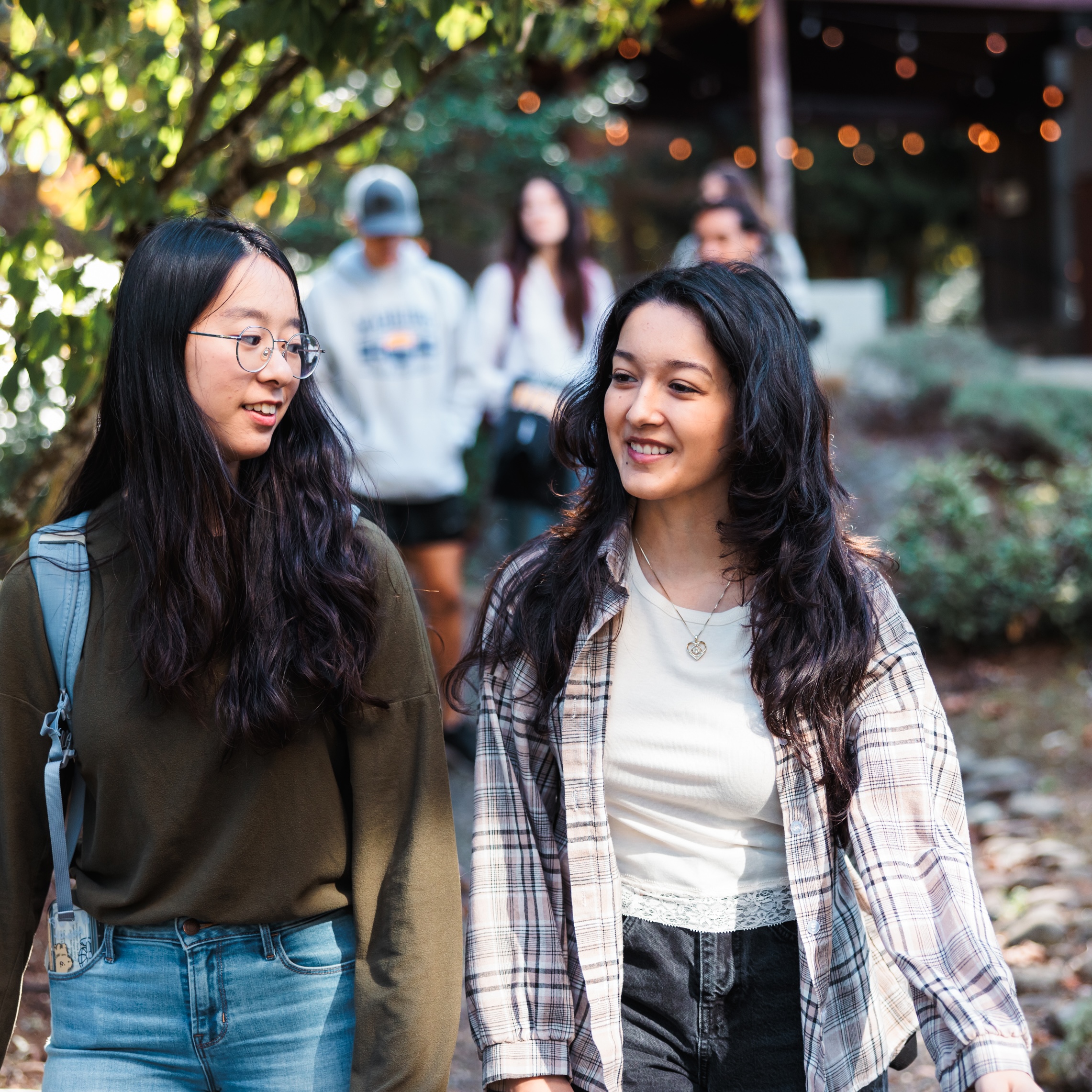 Two young women stroll down a tree-lined path, engaged in conversation and enjoying each other's company.