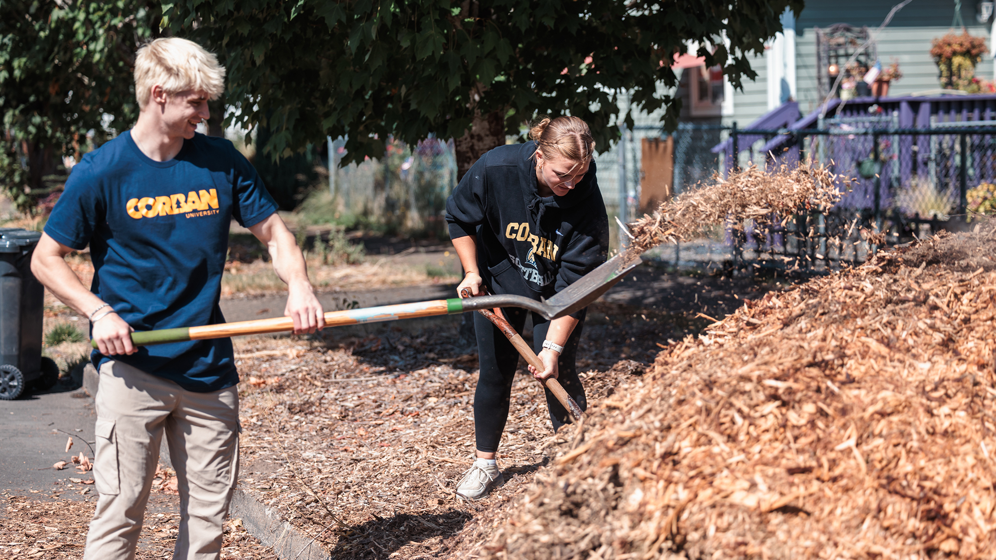 Two individuals working on landscaping with mulch in a yard for Serve Day.
