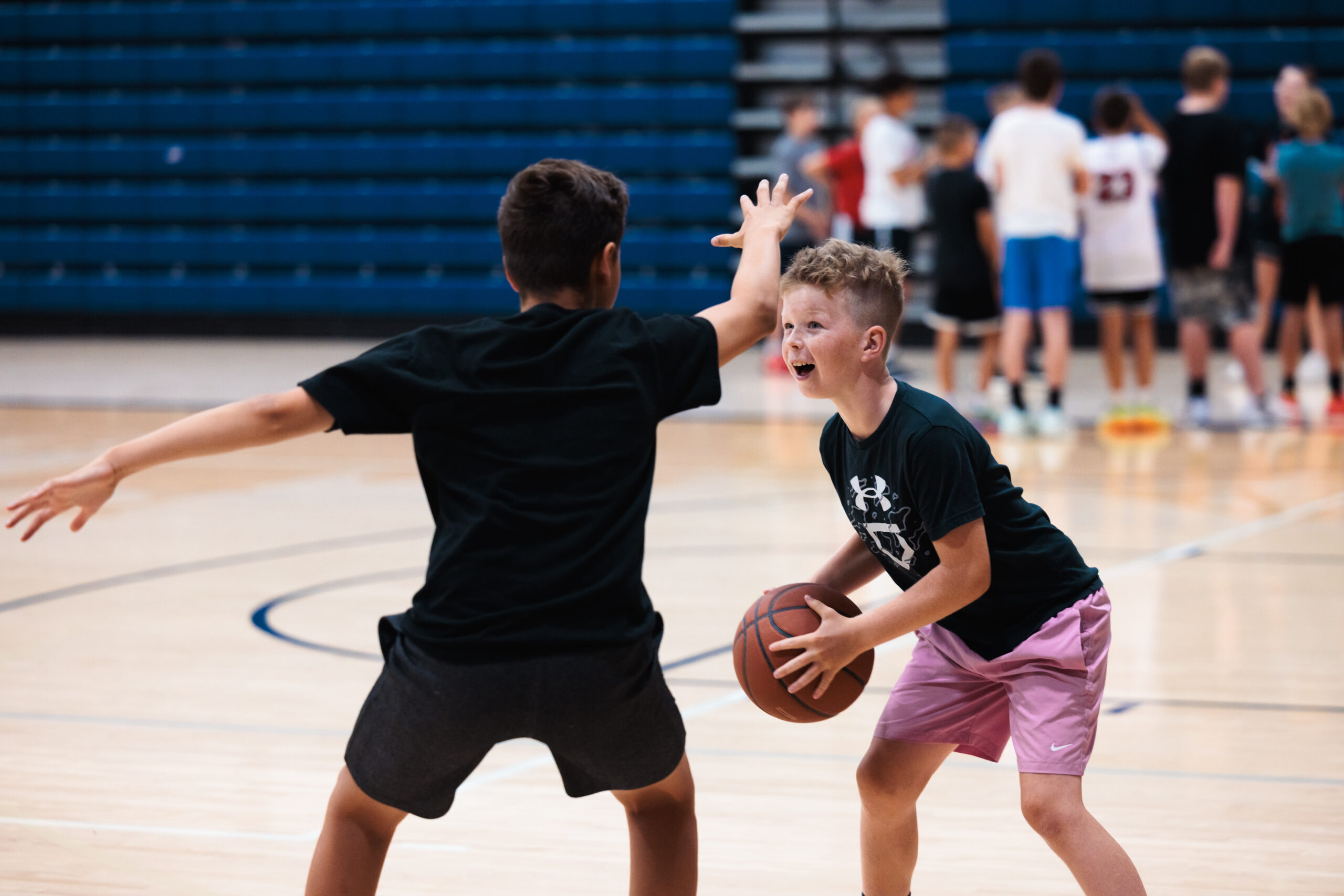 Two boys engaged in a game of basketball on a court at a youth camp, with one boy preparing to shoot the ball.