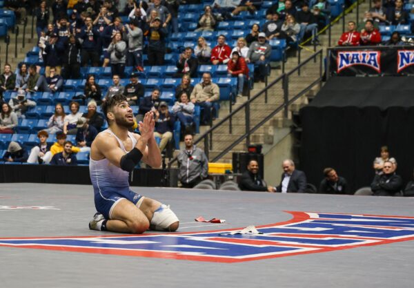 Wrestler David Rubio kneels with hands raised, expressing excitement on the mat.